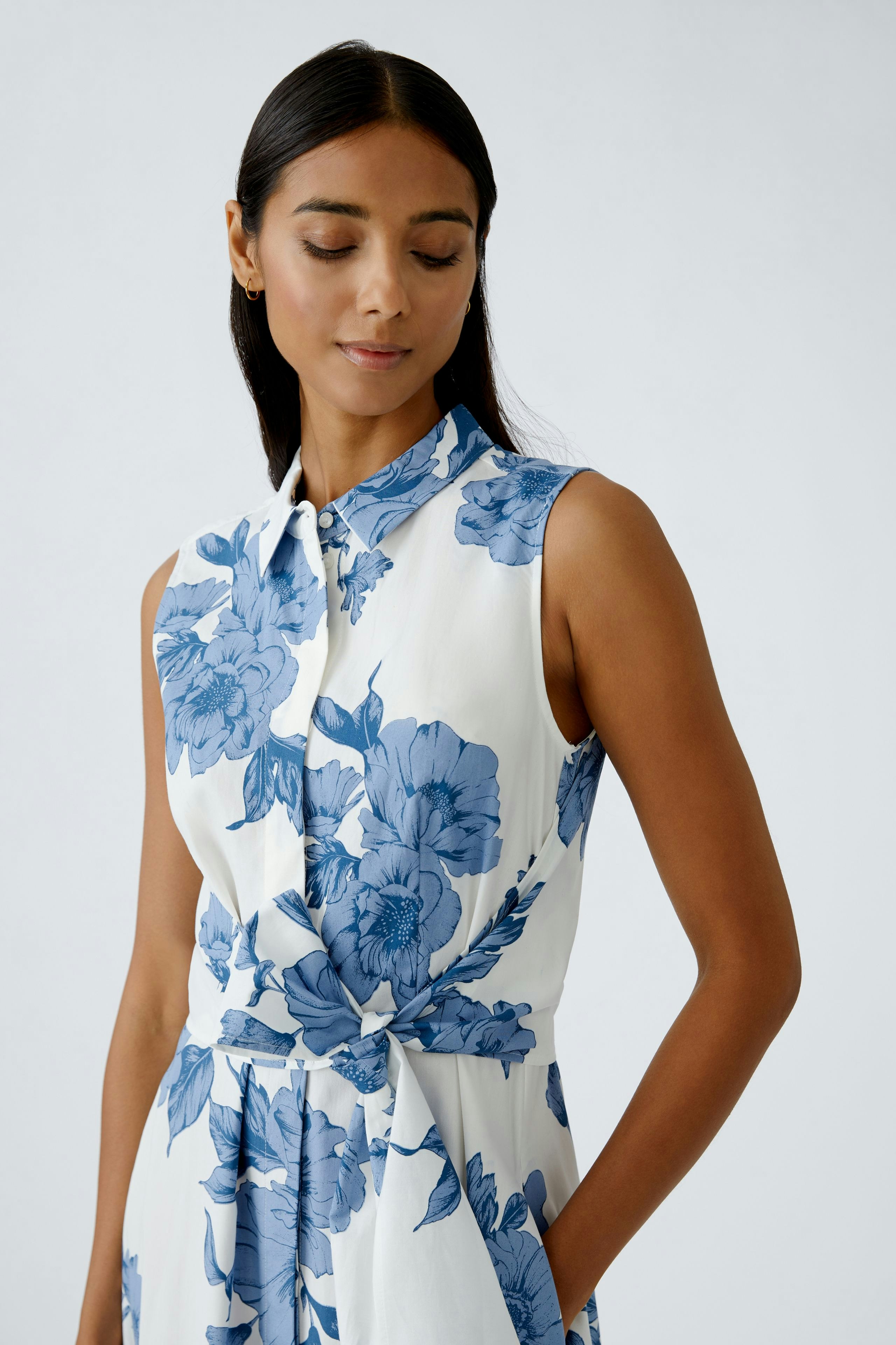 Floral maxi dress: Woman in a sleeveless dress with blue flowers, featuring a collar and a tied waist.