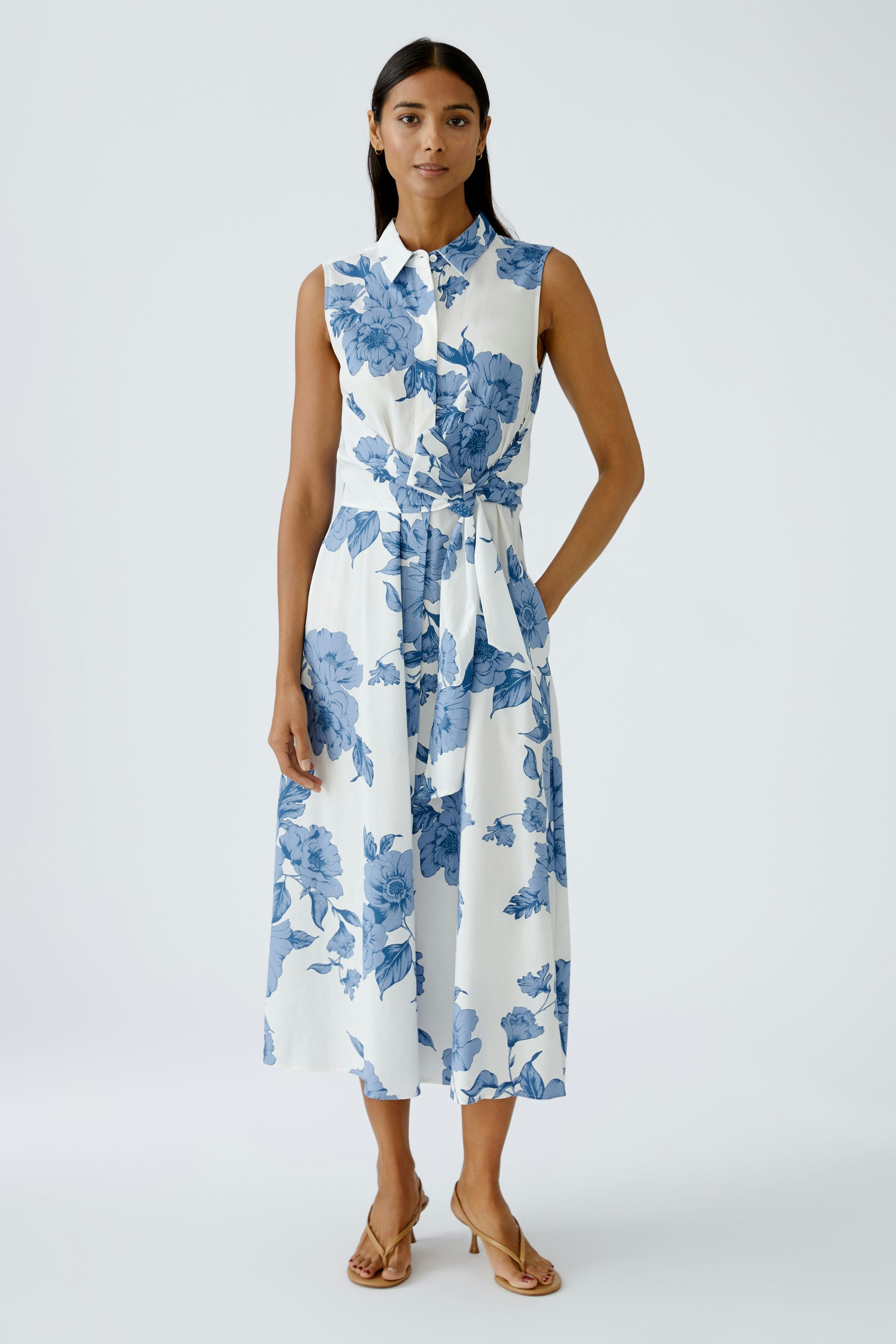 Floral maxi dress: Woman in a sleeveless dress with blue flowers, featuring a belted waist and button-up design.