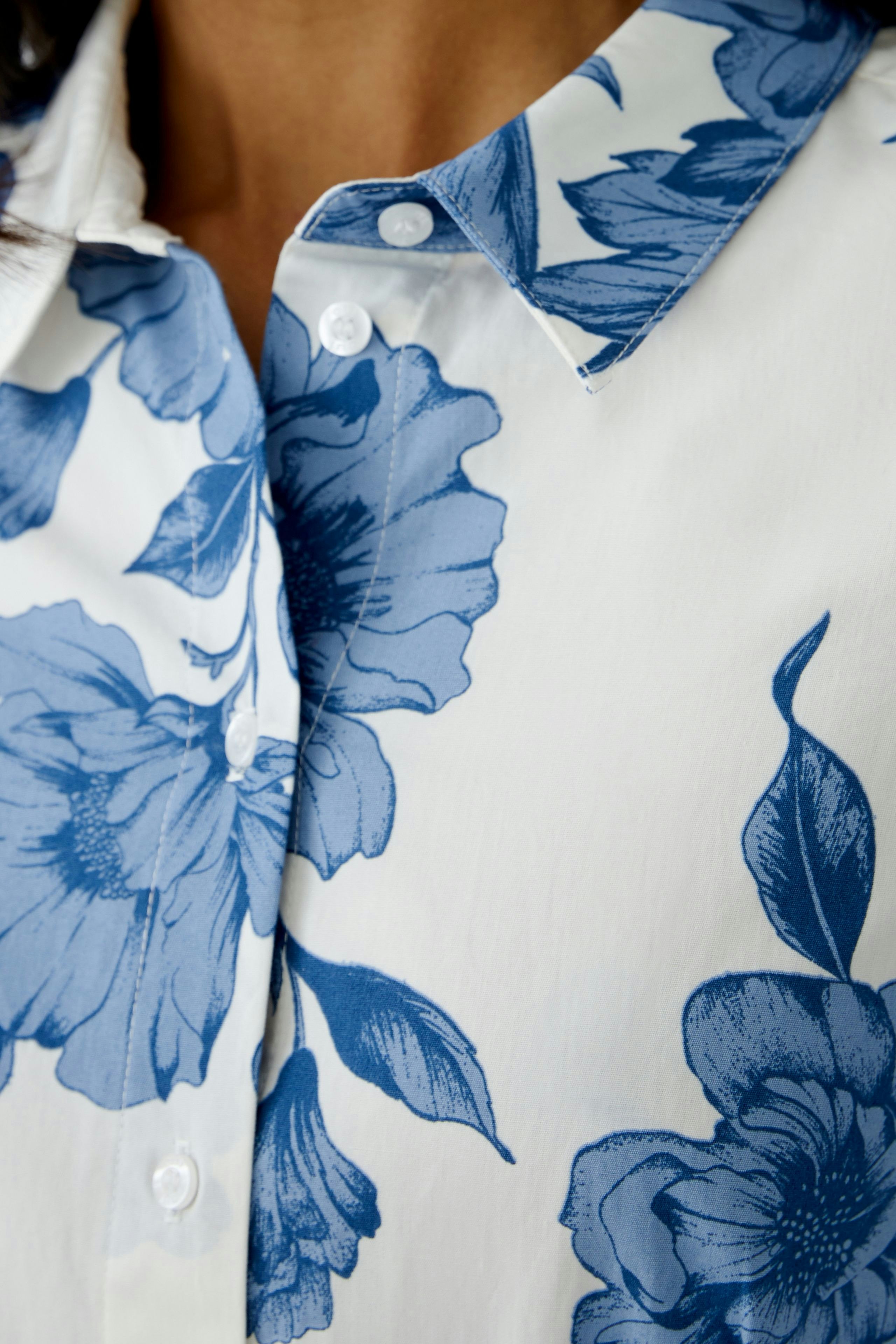 Floral midi dress: Close-up of a woman's shirt with blue floral patterns on a white background.