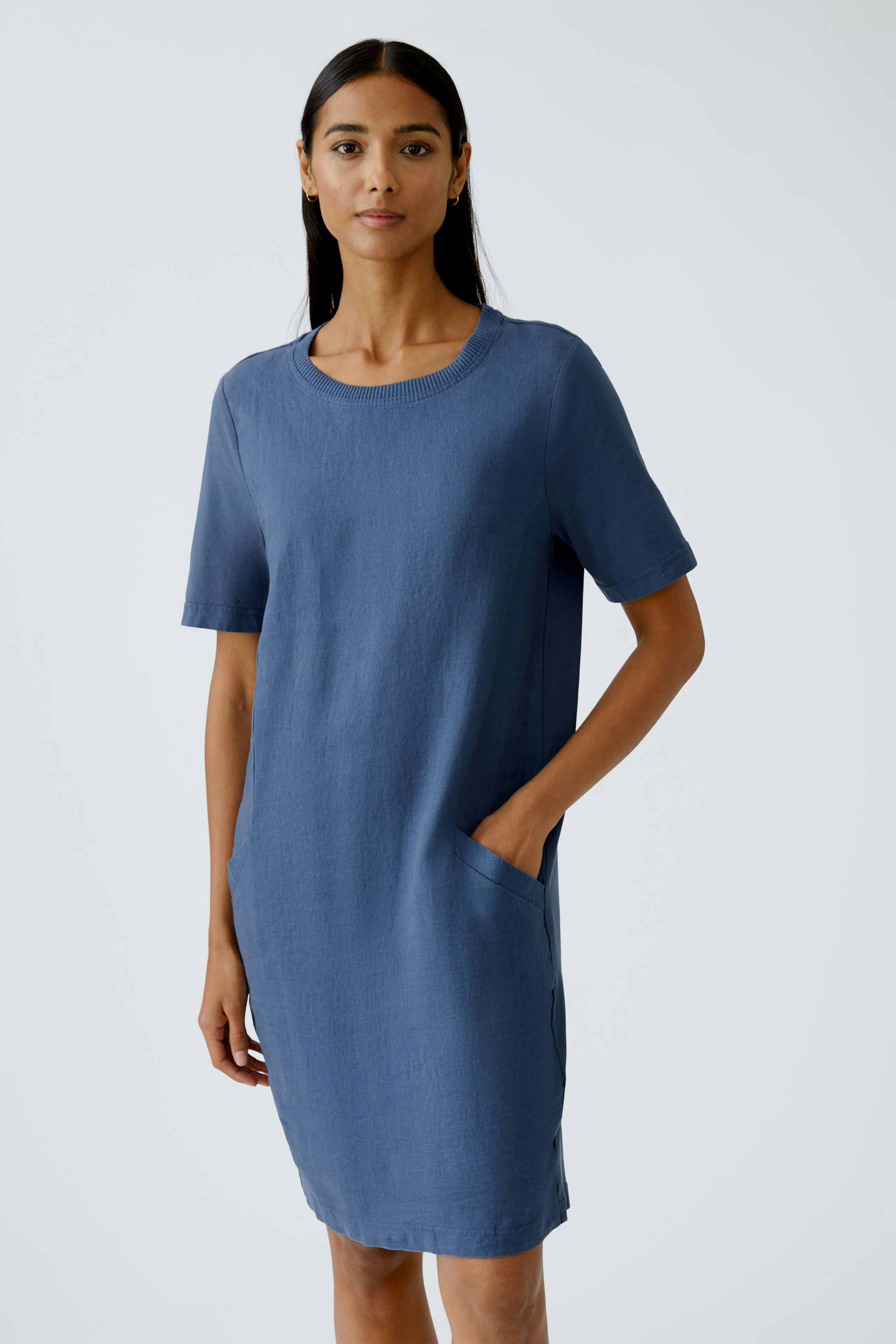 Casual women's dress: A woman in a blue short-sleeve dress with pockets stands confidently.
