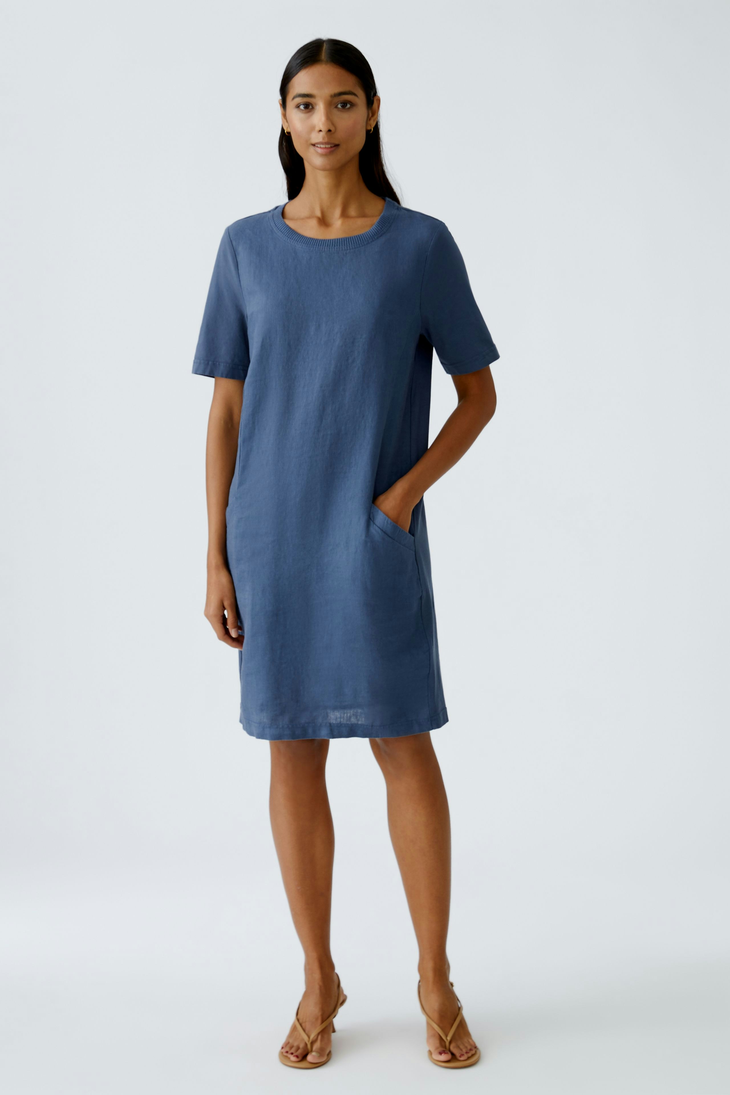 Casual women's dress: A woman in a blue short-sleeve dress with pockets stands confidently.