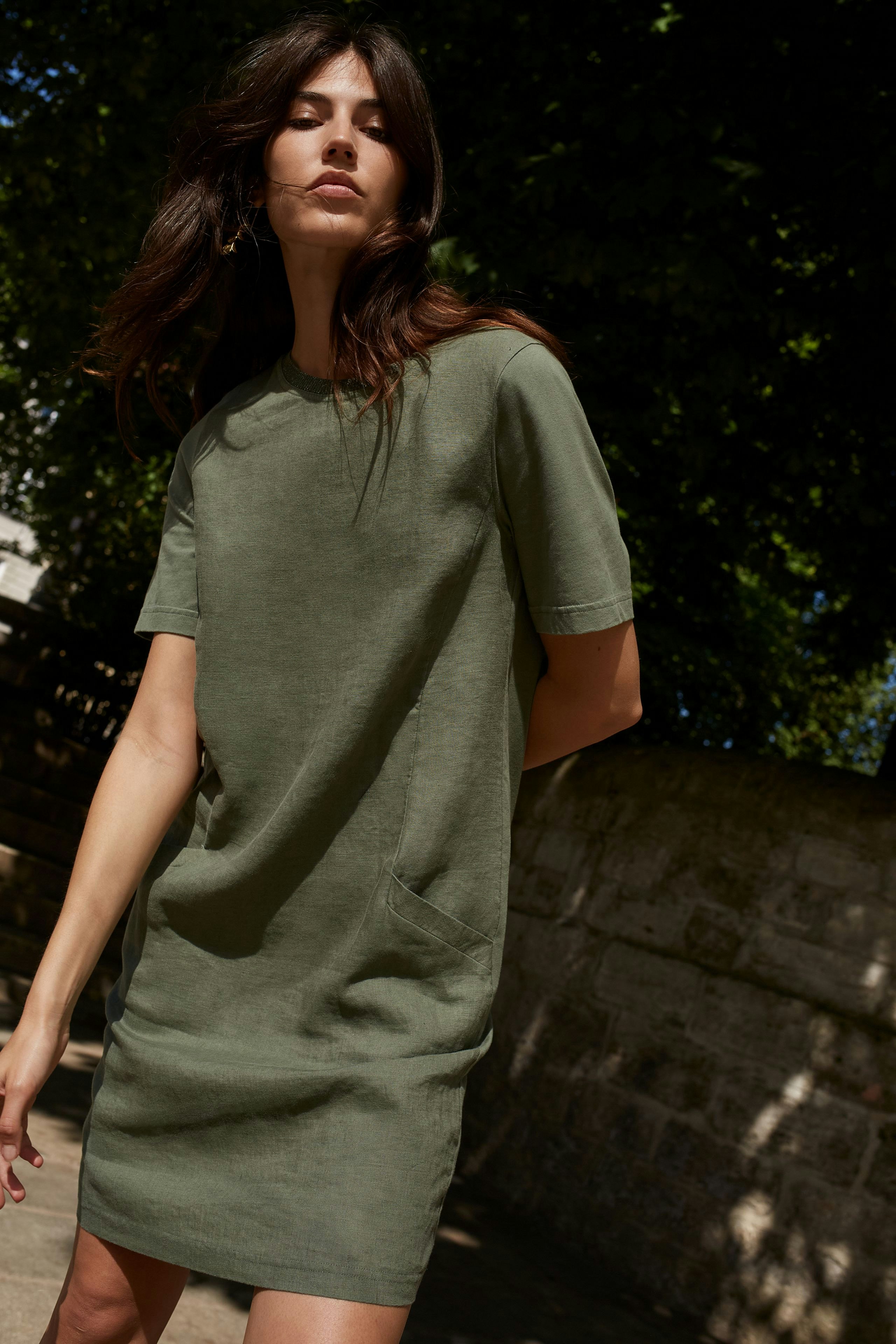 Casual women's dress: A woman in a short-sleeved olive green dress with pockets stands confidently outdoors.