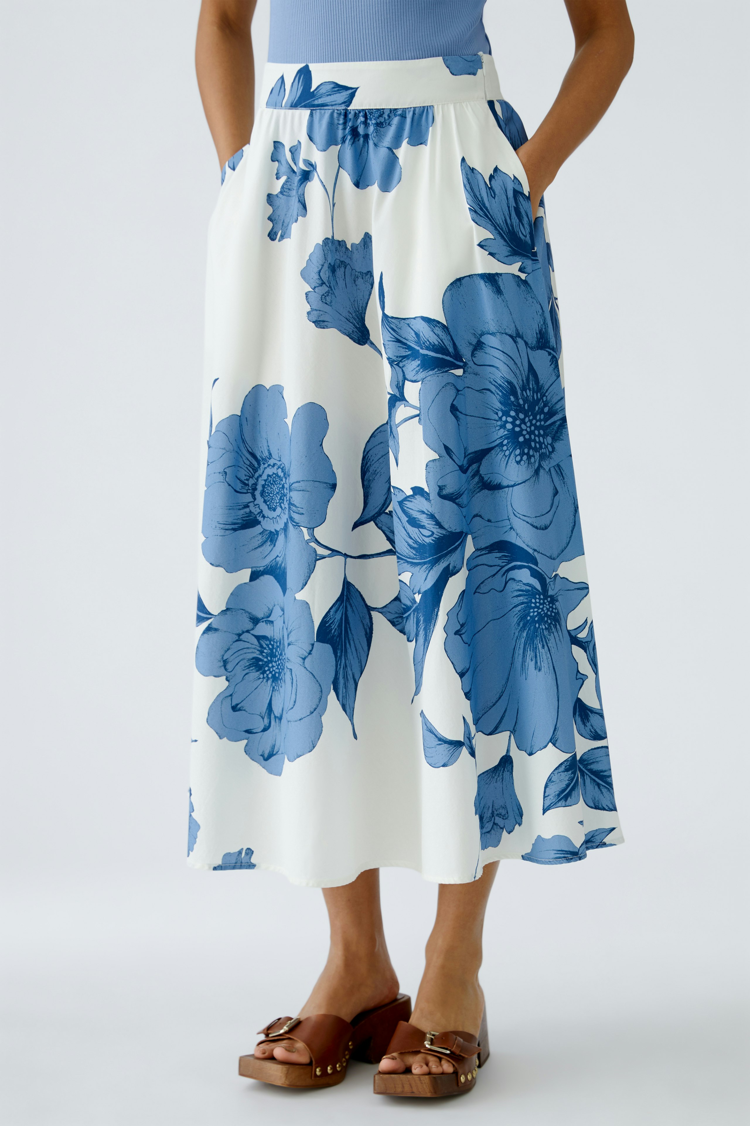 Floral A-line skirt: Woman in a flowy skirt with blue flowers, featuring pockets and a comfortable fit.