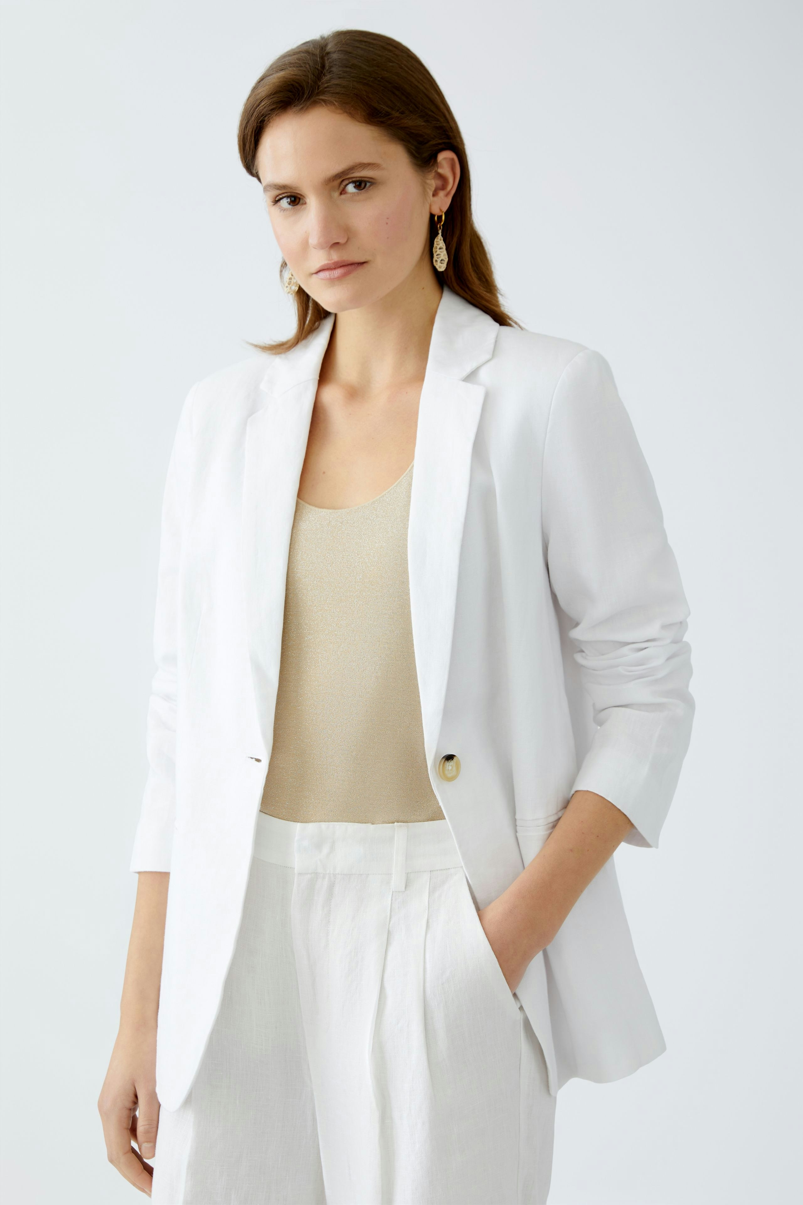 Eleganter Damen-Blazer: Frau in weißem Blazer über einem goldenen Top, kombiniert mit hellen Hosen.