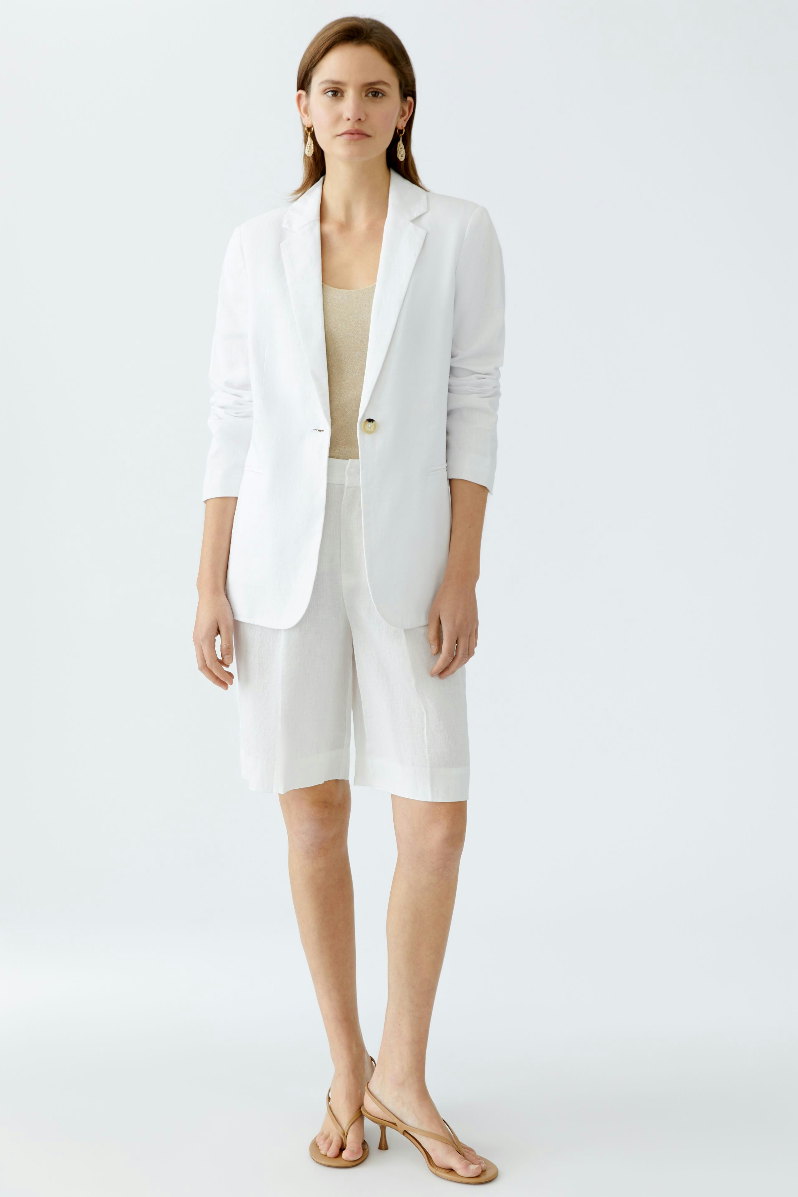 Eleganter Damen-Blazer: Frau in weißem Blazer über einem hellen Top, kombiniert mit lässigen Shorts.