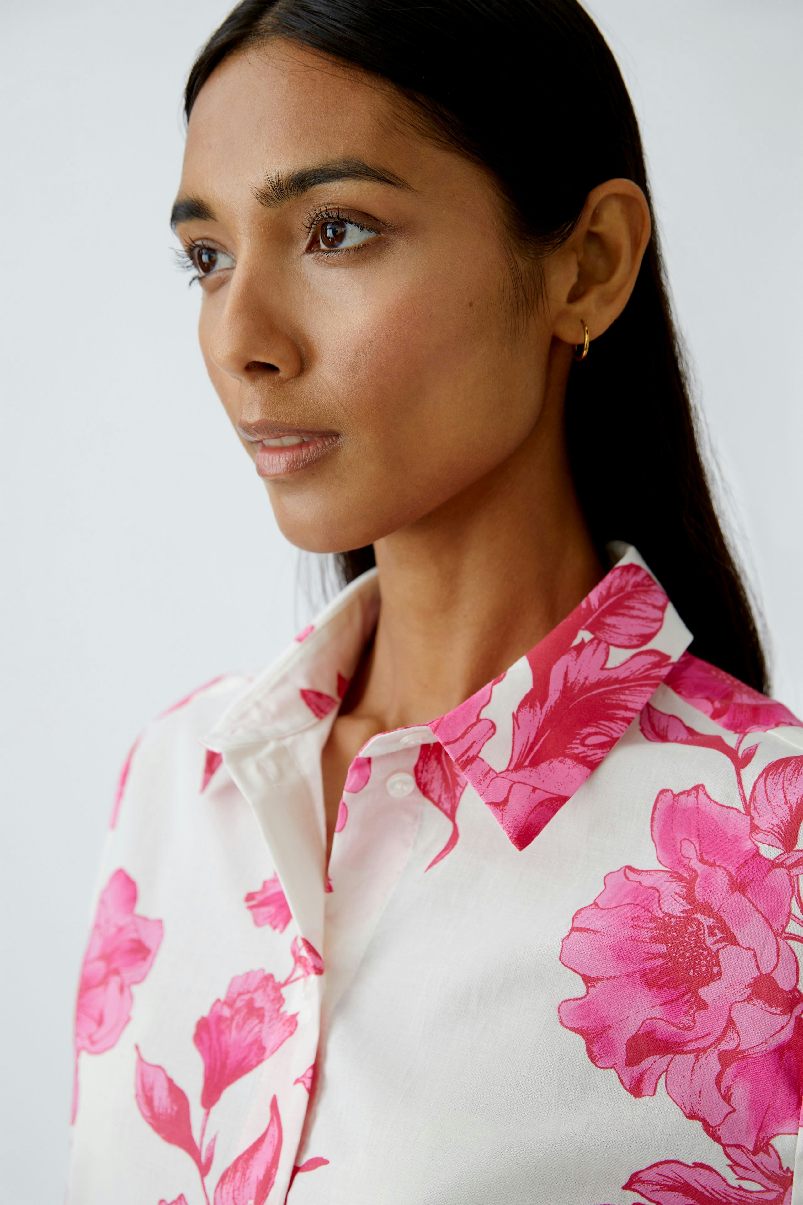 Damen-Bluse: Frau trägt eine Bluse mit pinken Blumen auf hellem Hintergrund.
