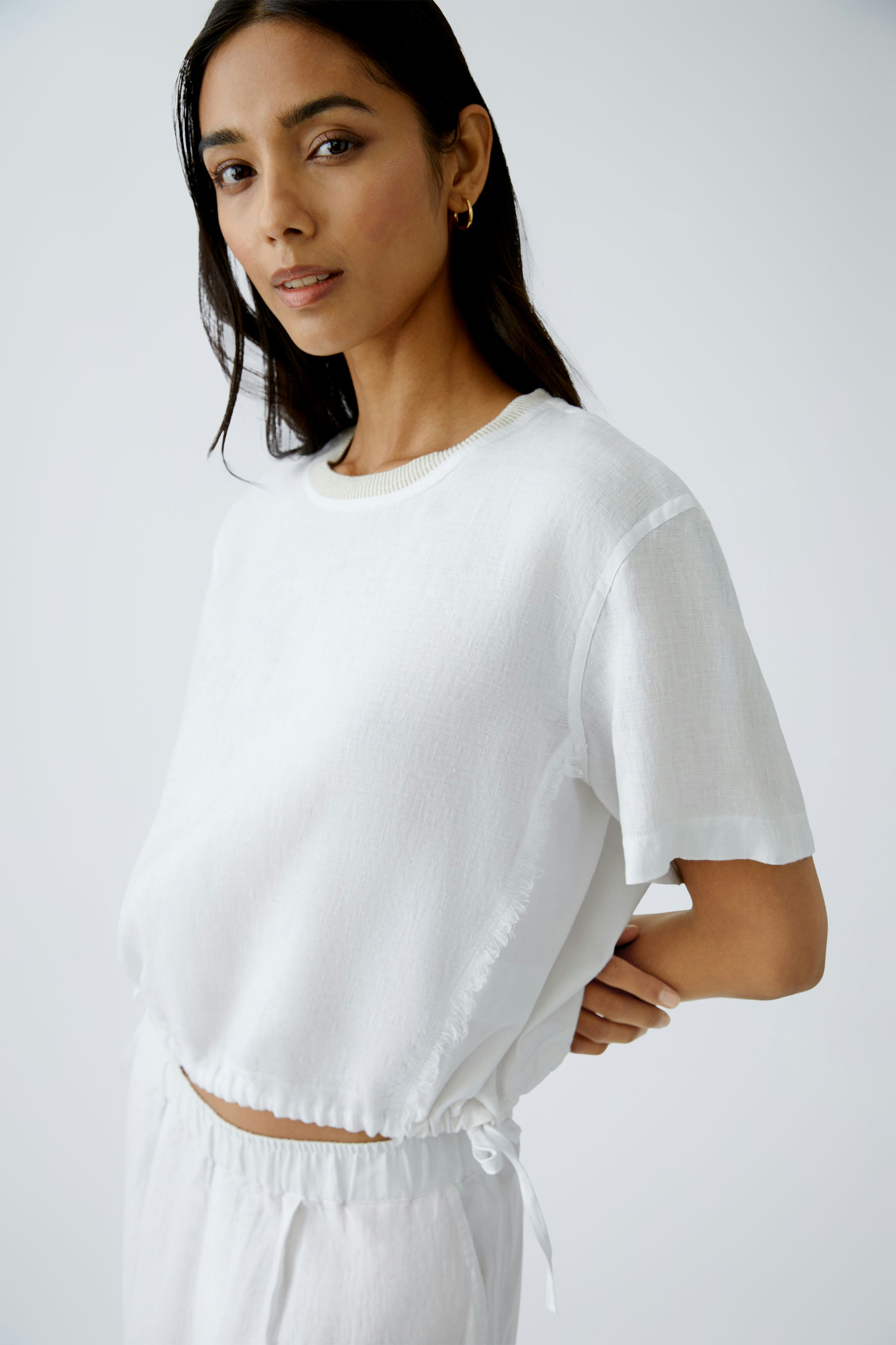 Luftiges Blusenshirt: Junge Frau in weißem, lässigem Shirt mit fransigen Abschlüssen und lockerer Passform.