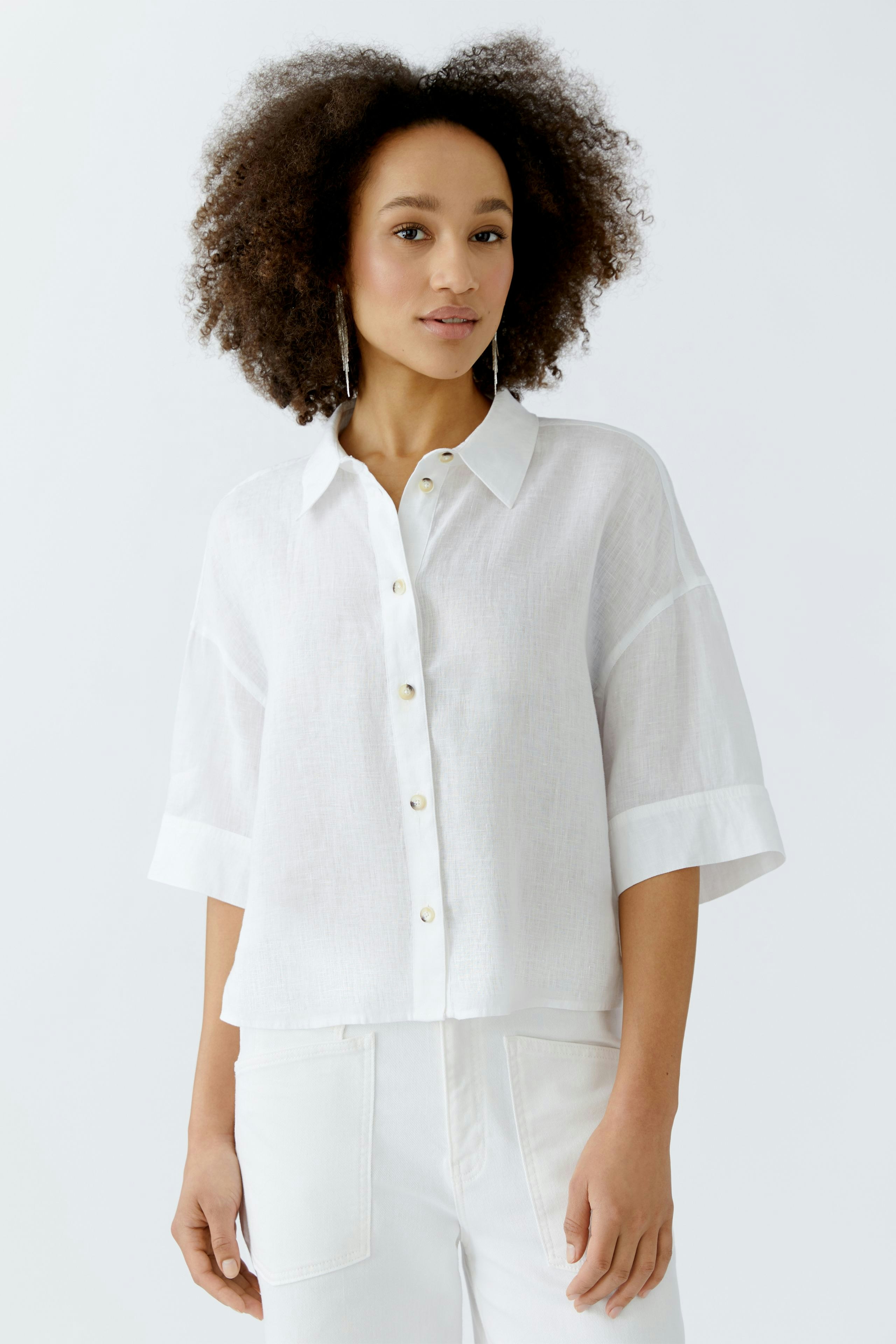 Casual women's blouse: A woman in a white button-up blouse with rolled sleeves, paired with light pants.