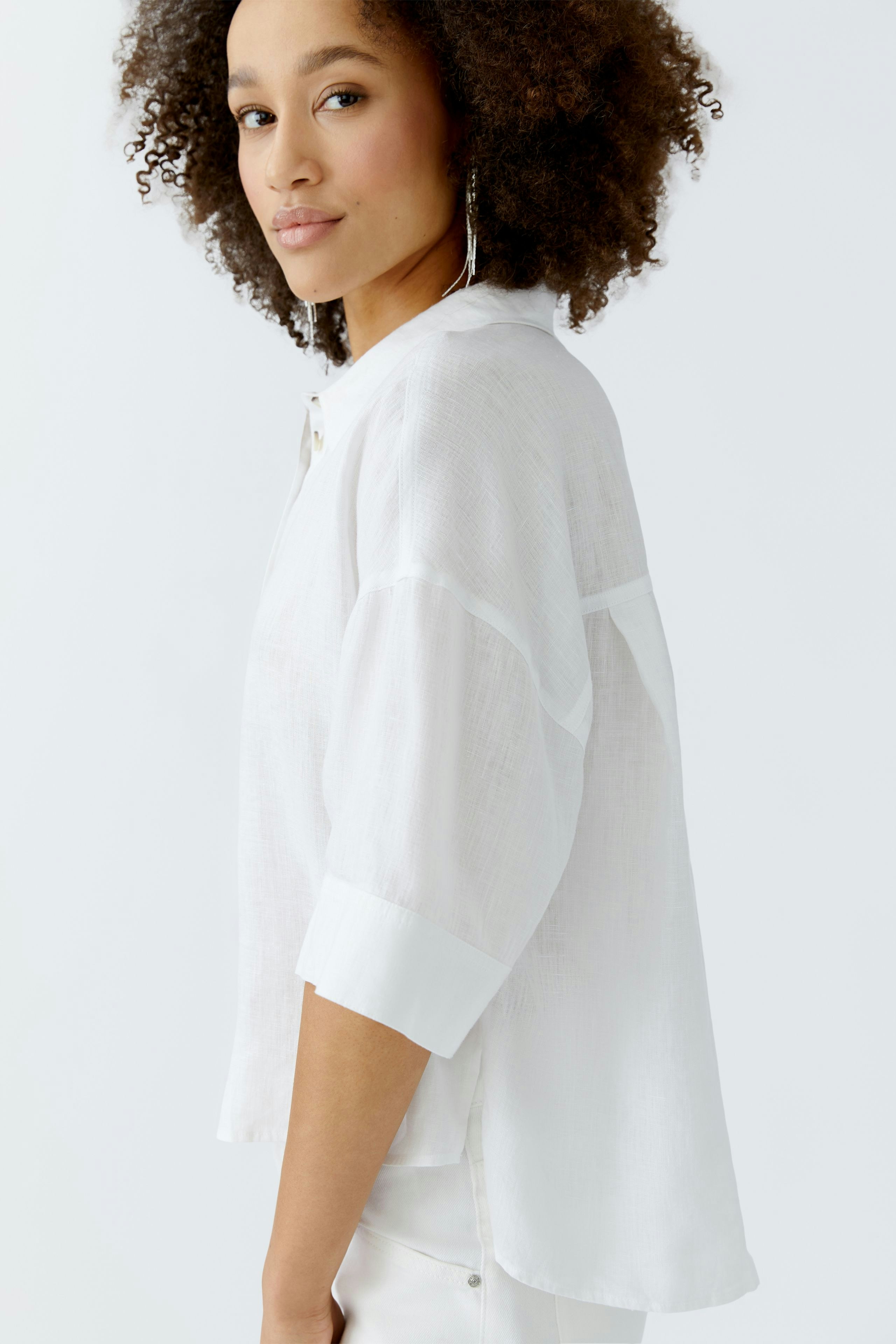 Casual women's blouse: Young woman in a white, loose-fitting blouse with rolled sleeves, smiling confidently.