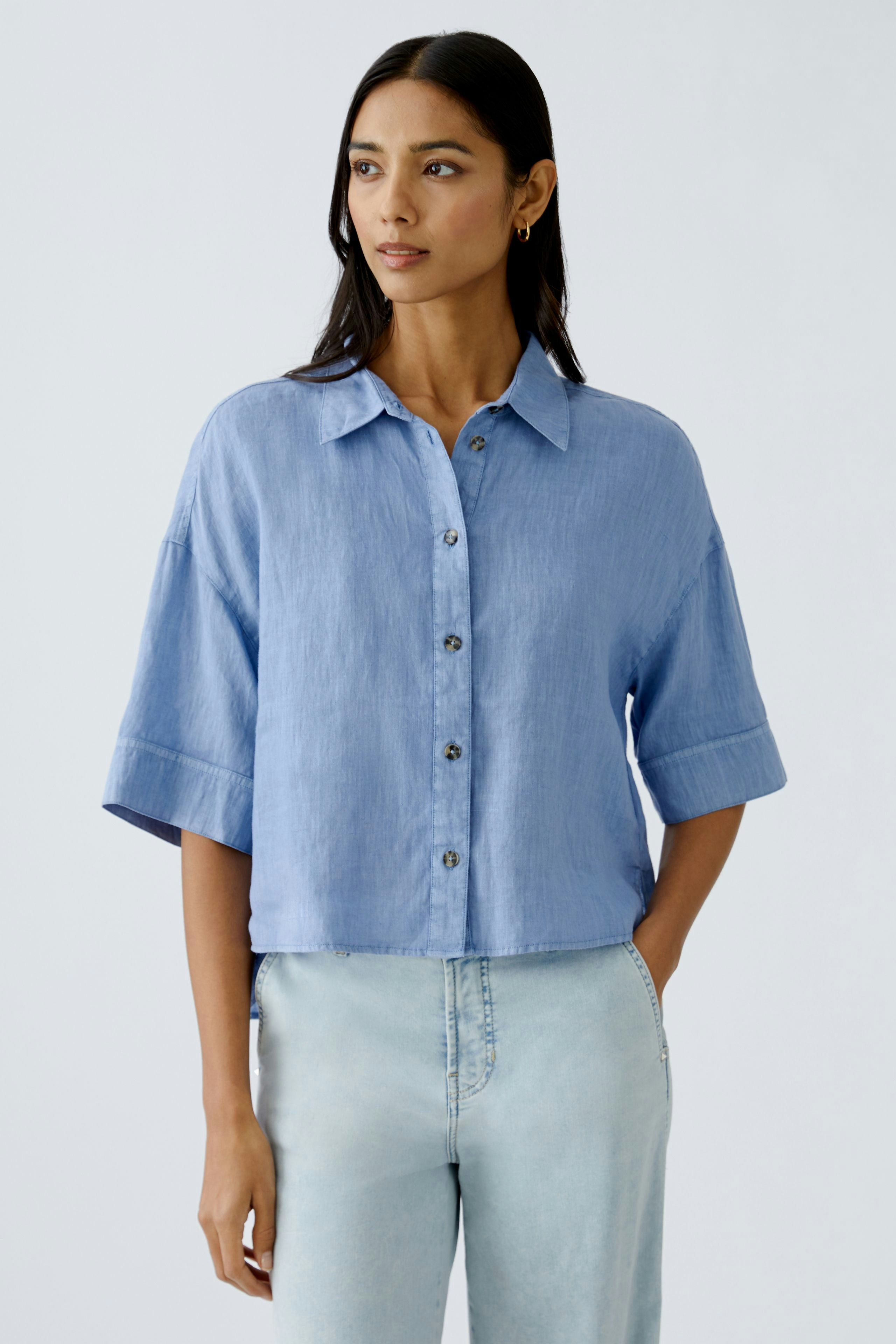 Helle Damen-Bluse: Frau in blauer, kurzärmeliger Bluse mit Knöpfen und lässigem Schnitt.