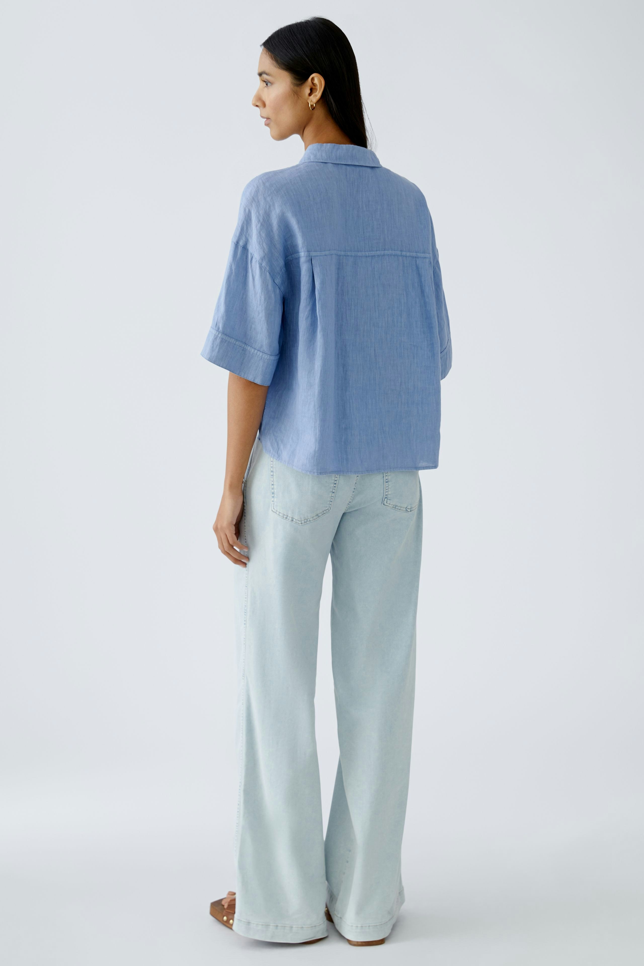 Luftige Damen-Bluse: Frau in blauer Bluse mit kurzen Ärmeln und lässigen Jeans von hinten.