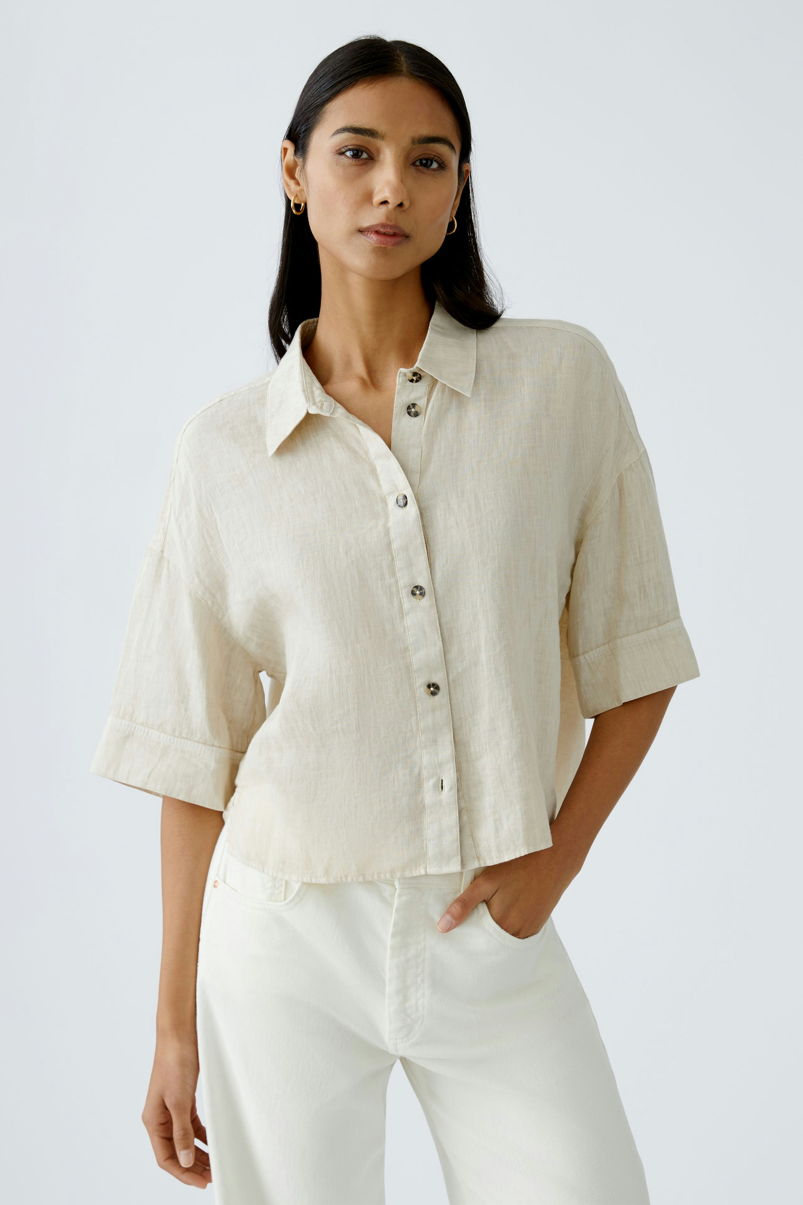 Stylish women's blouse: A woman in a light beige button-up blouse with rolled sleeves.