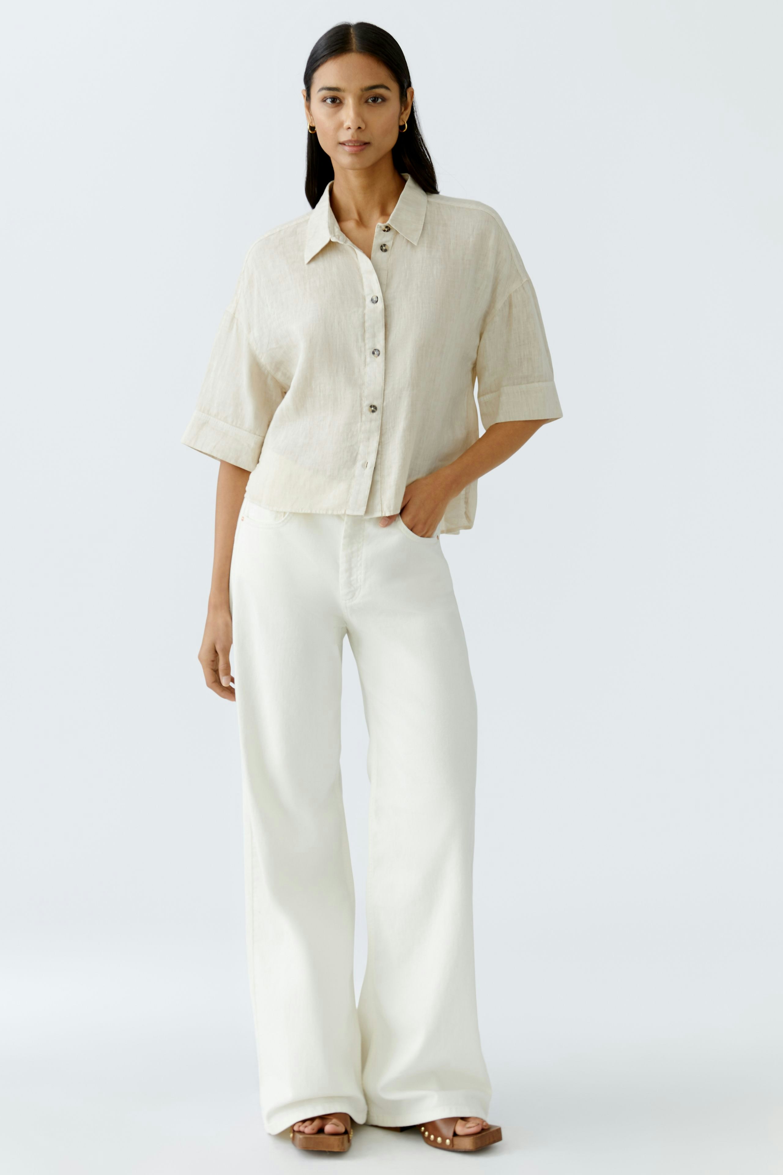 Stylish women's blouse: A woman in a light beige button-up blouse paired with white wide-leg pants.