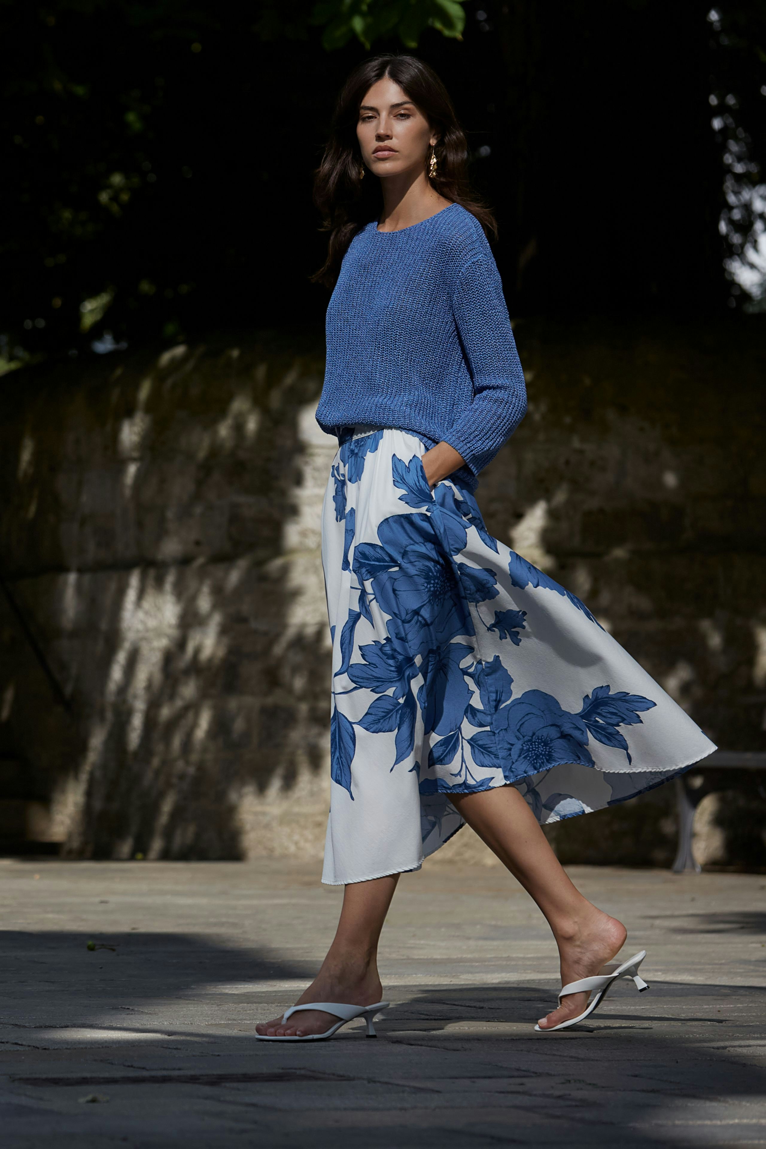 Stylish women's pullover: A woman in a blue knitted pullover sits confidently on a bench.