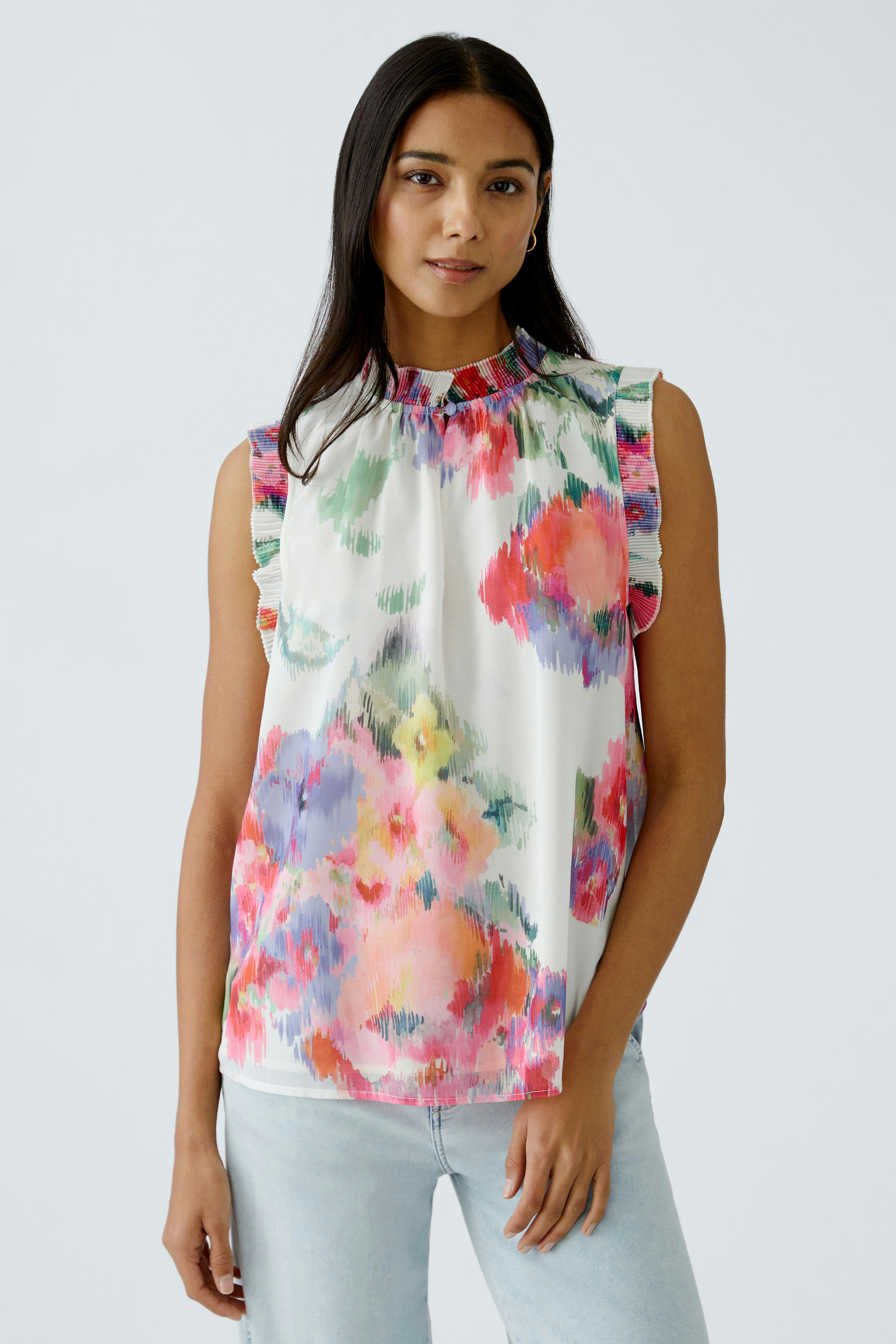 Feminine Bluse: Frau trägt eine farbenfrohe, ärmellose Bluse mit Rüschen und floralem Muster.