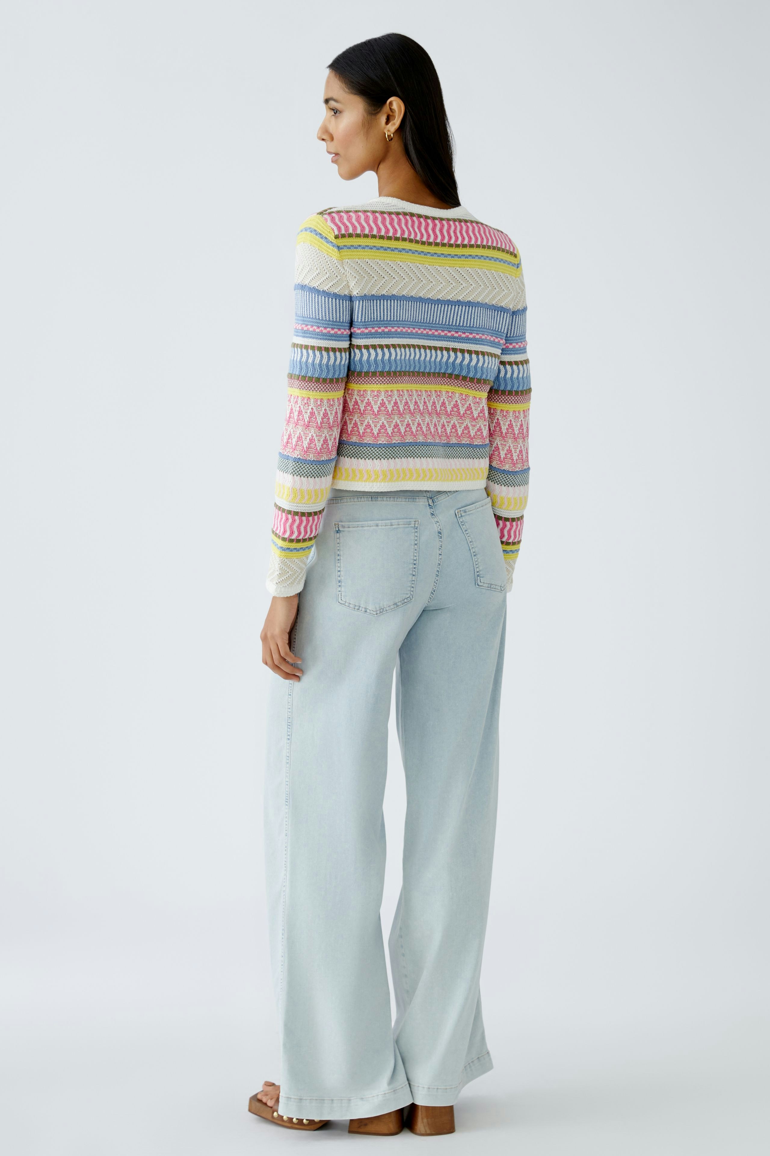 Bunte Damen-Strickjacke: Frau mit farbenfrohem, gemustertem Pullover und lässigen Jeans von hinten.