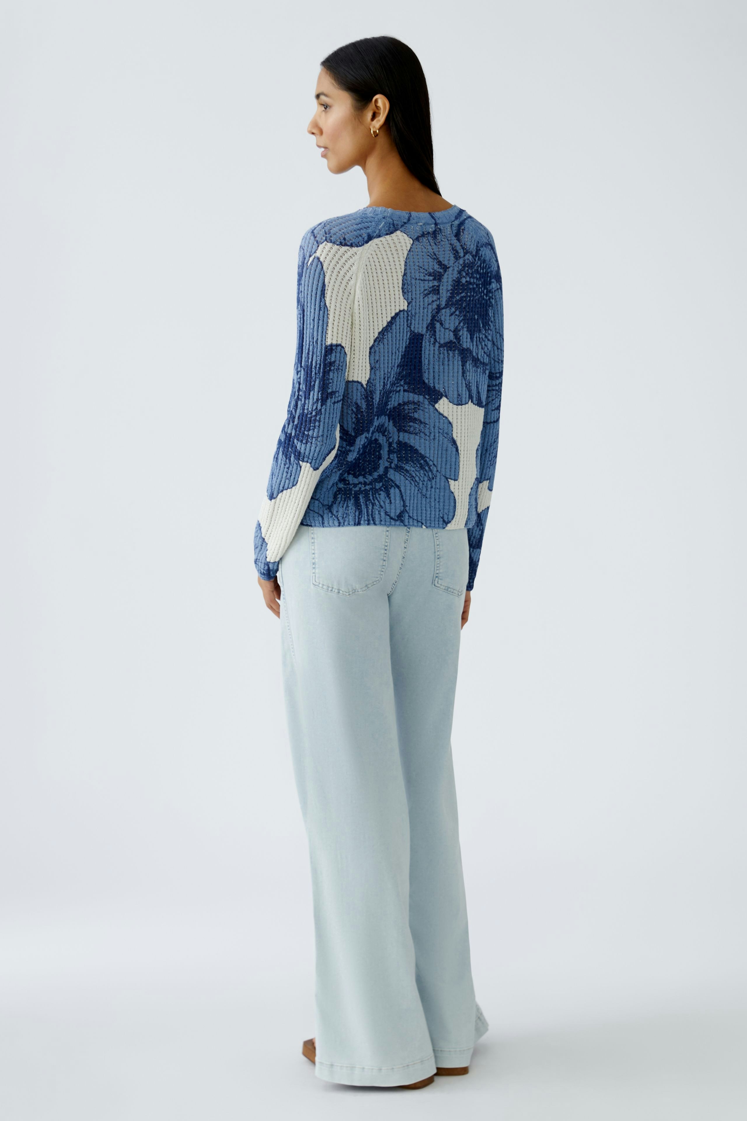 Damen-Pullover: Frau in blauem, floralem Strickpullover mit lässigen Jeans von hinten.