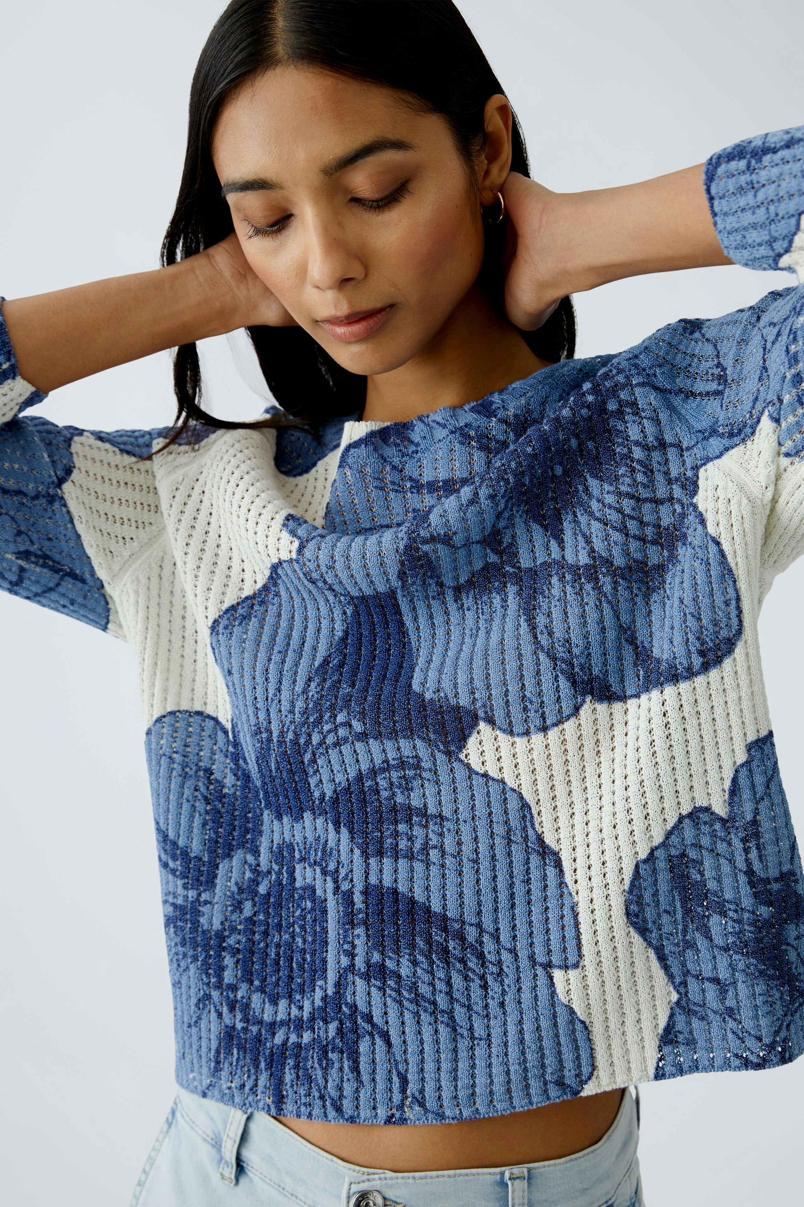 Damen-Pullover: Frau in blau-weißem, floralem Strickpullover mit lässigem Schnitt.