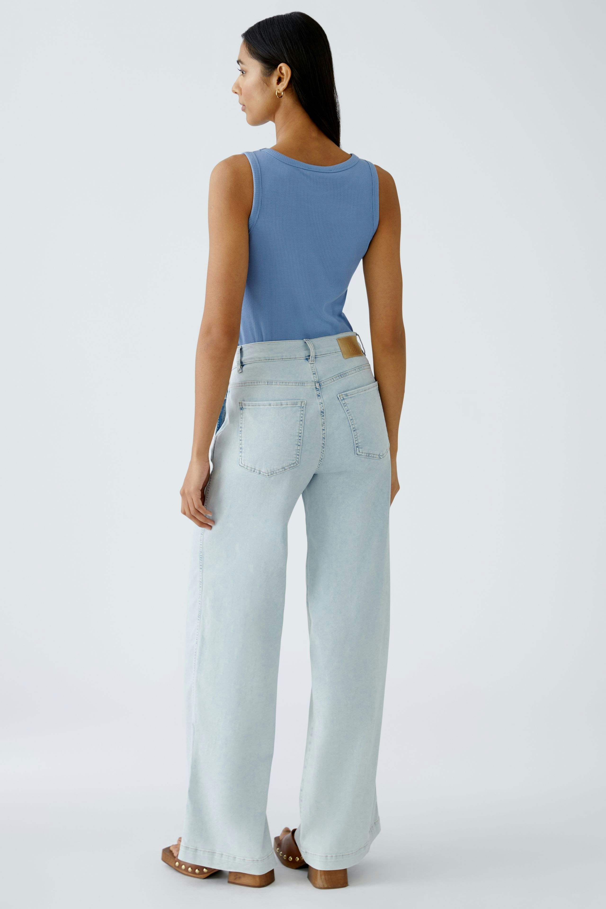 Damen Jeans Flared: Frau in hellblauen, weiten Jeans mit lässigem Schnitt und hohem Bund von hinten.