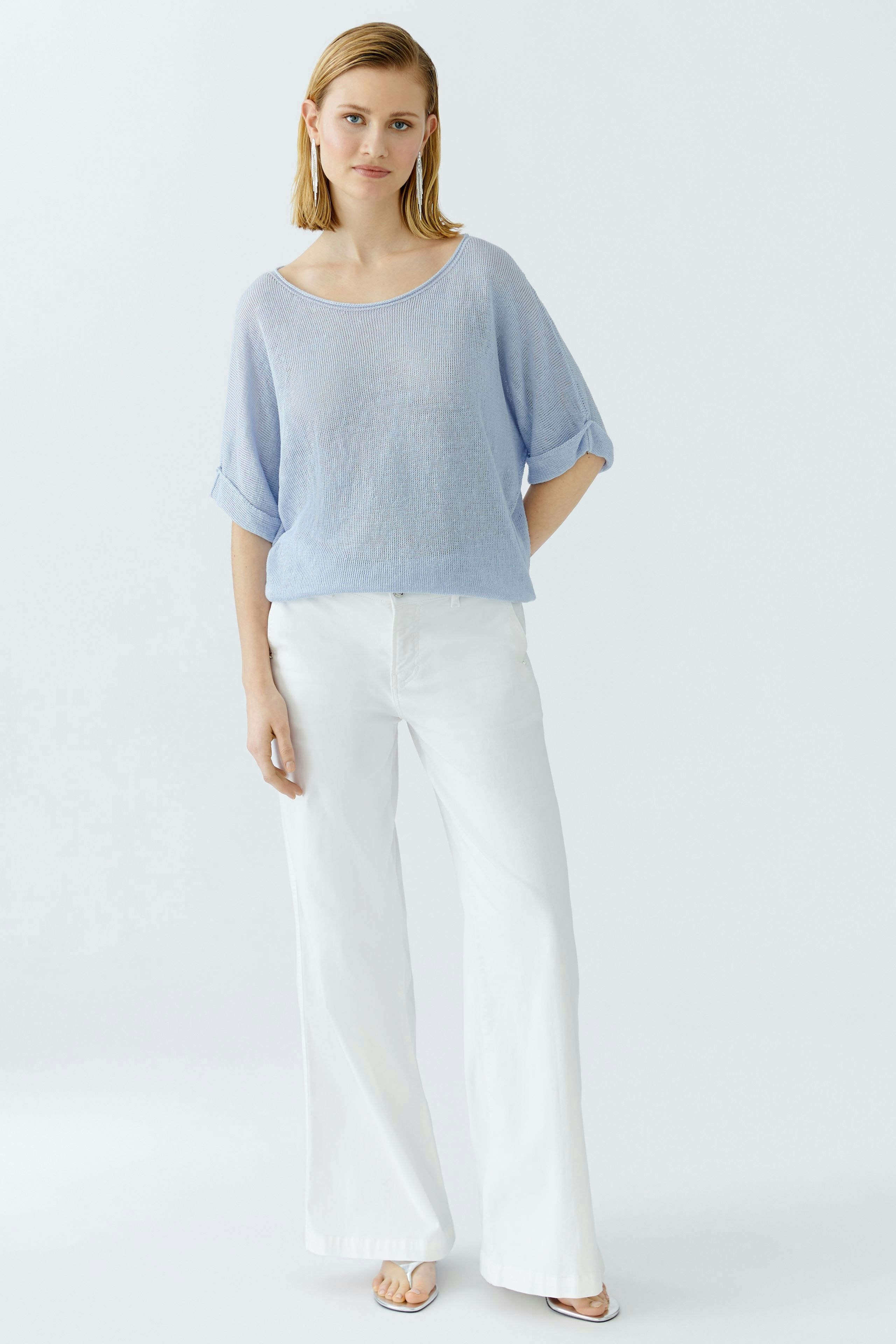 Casual women's pullover: Young woman in a light blue pullover with rolled sleeves and white pants.