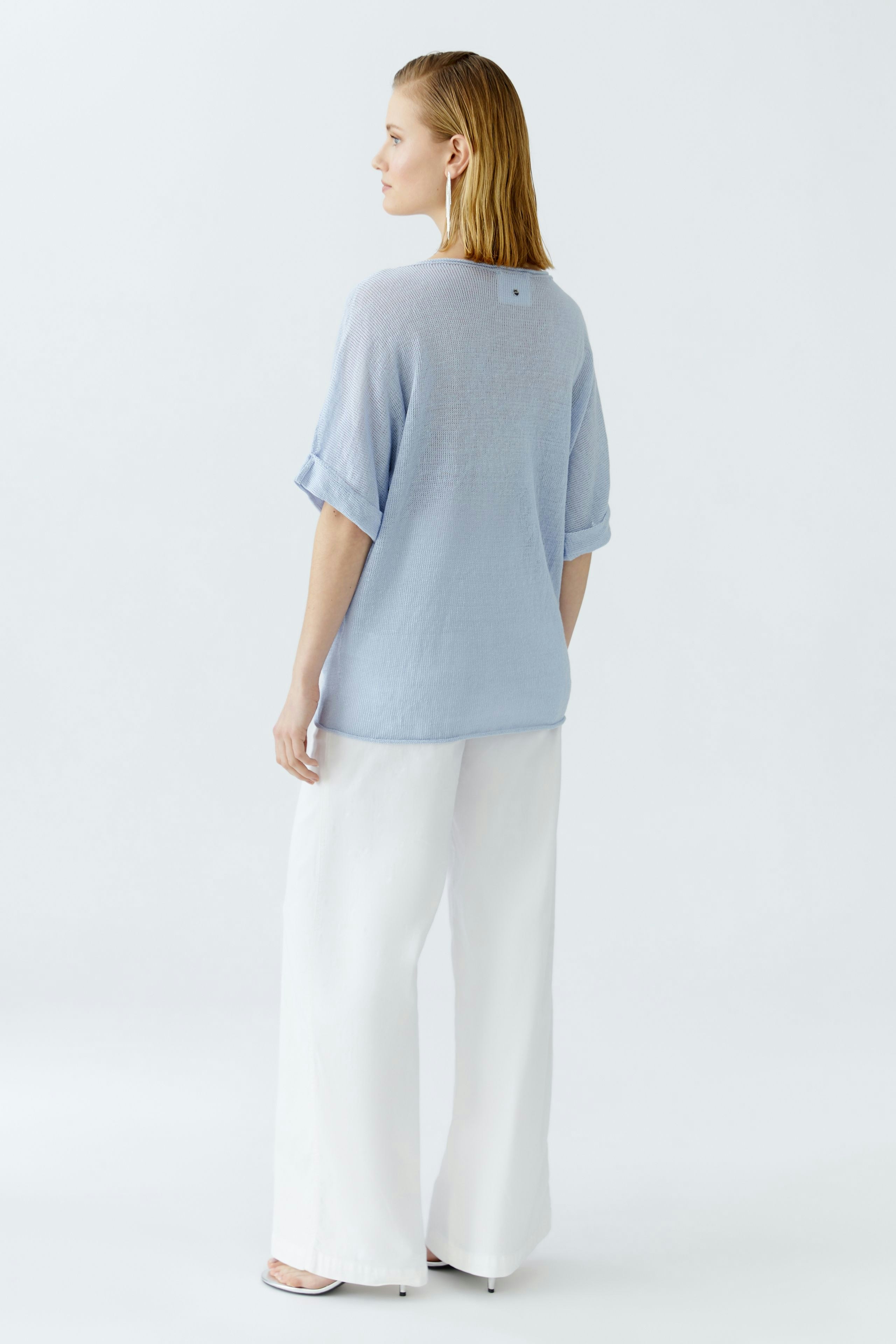 Casual women's pullover: Woman in a light blue pullover with rolled sleeves, paired with wide white pants.