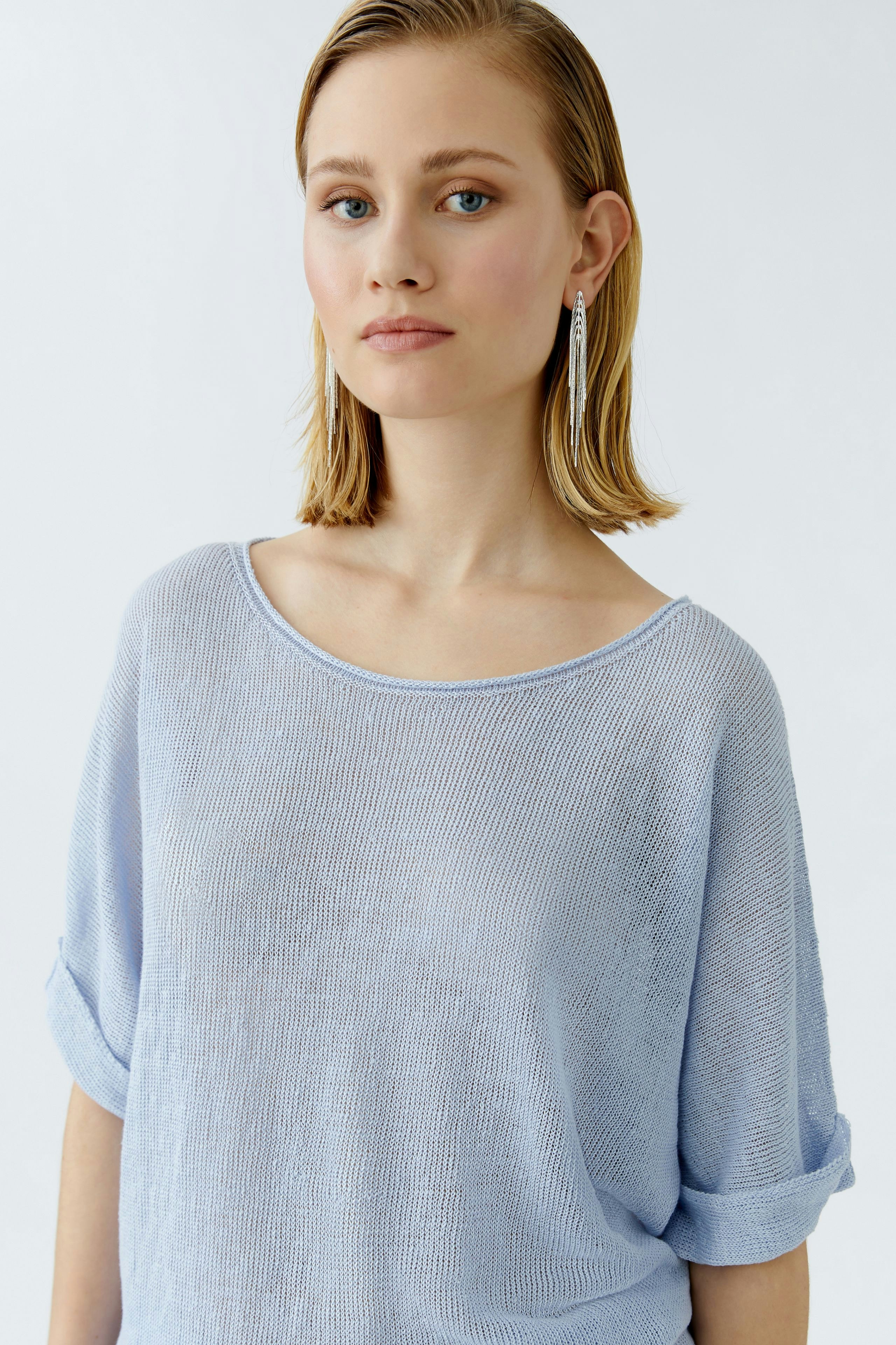 Casual women's pullover: Woman in a light blue pullover with rolled sleeves, looking confidently at the camera.