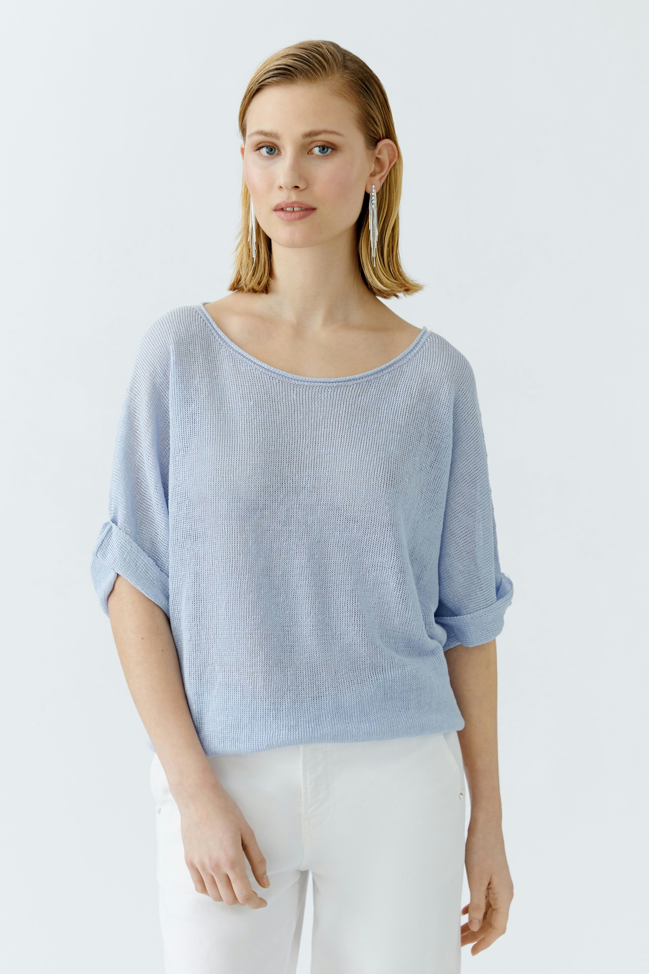 Casual women's pullover: A woman in a light blue pullover with rolled sleeves, looking relaxed.
