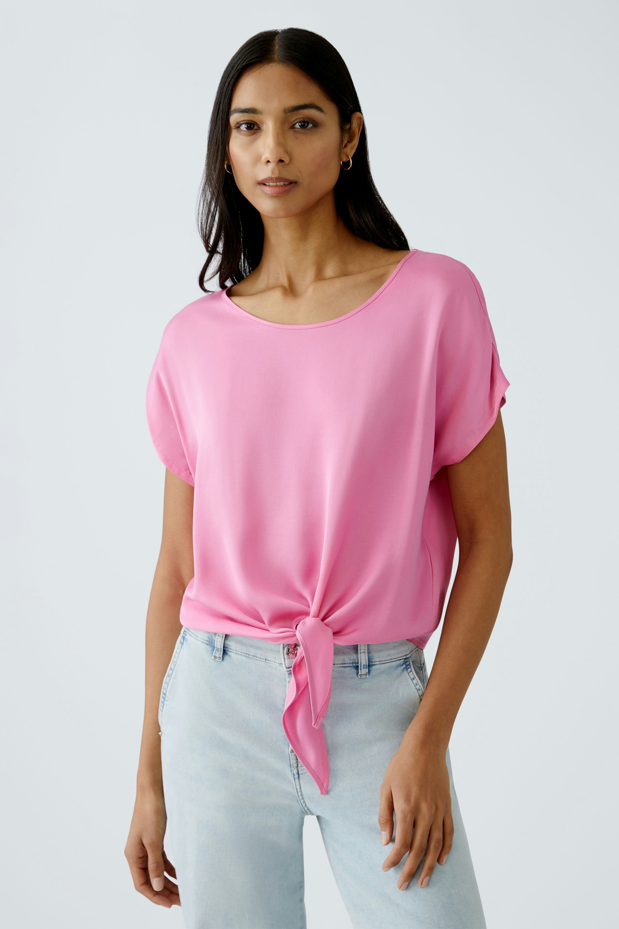 Stylish women's blouse: A woman in a pink blouse with a knot detail, paired with light jeans.