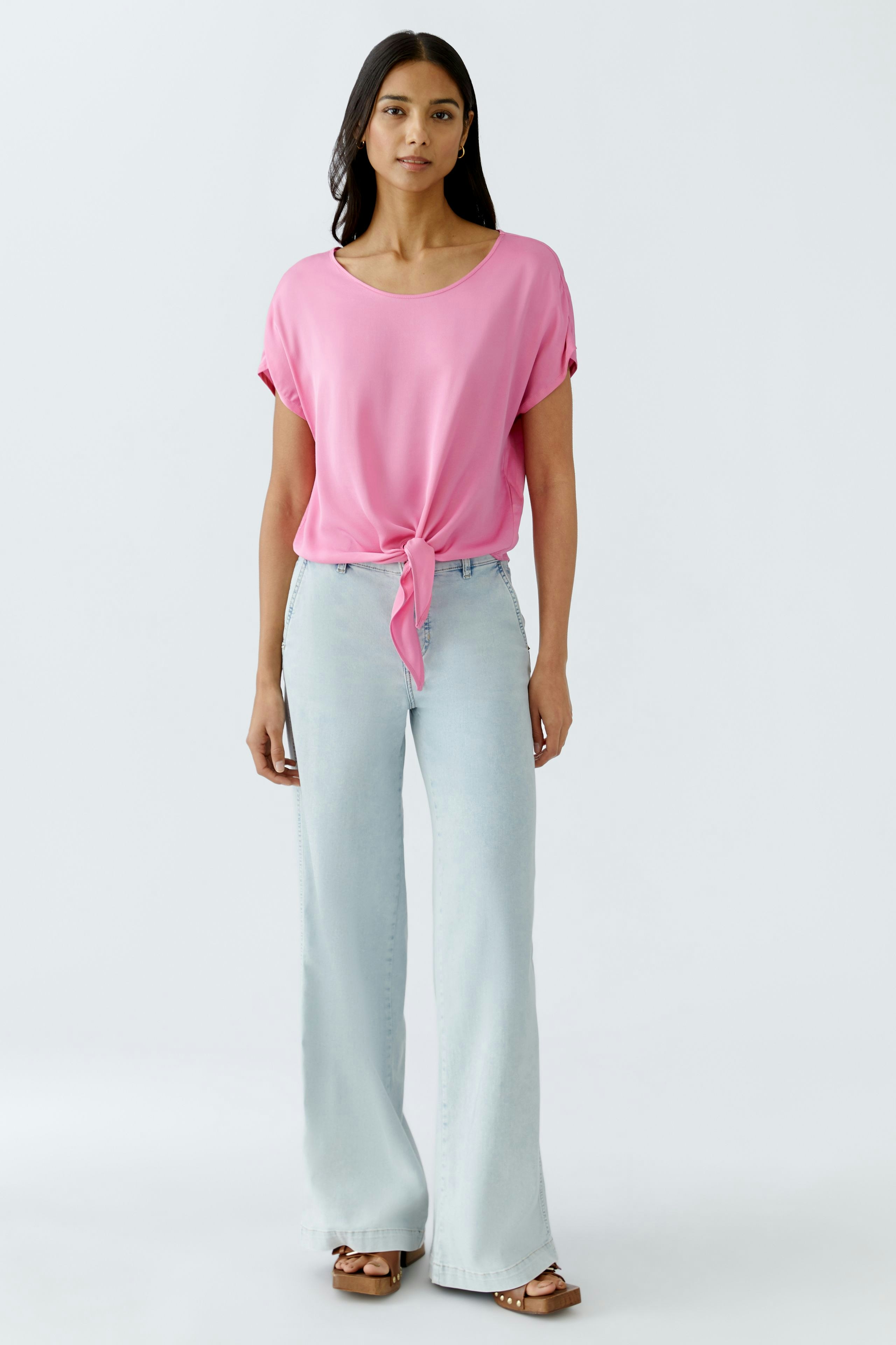 Stylish women's blouse: A woman in a pink blouse with a knotted front and light blue jeans.