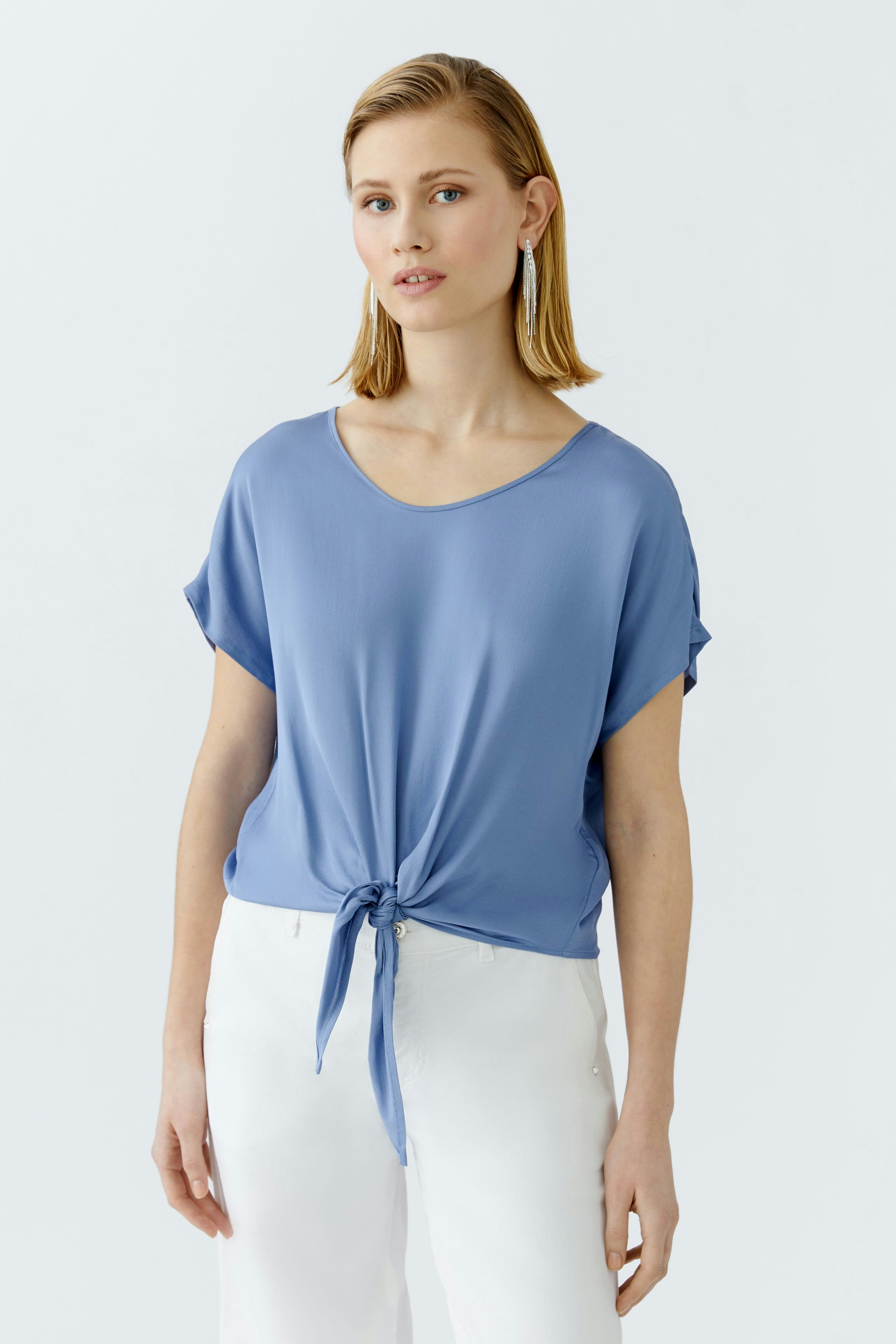 Casual women's blouse: A woman in a blue tie-front top paired with white pants, exuding a relaxed vibe.