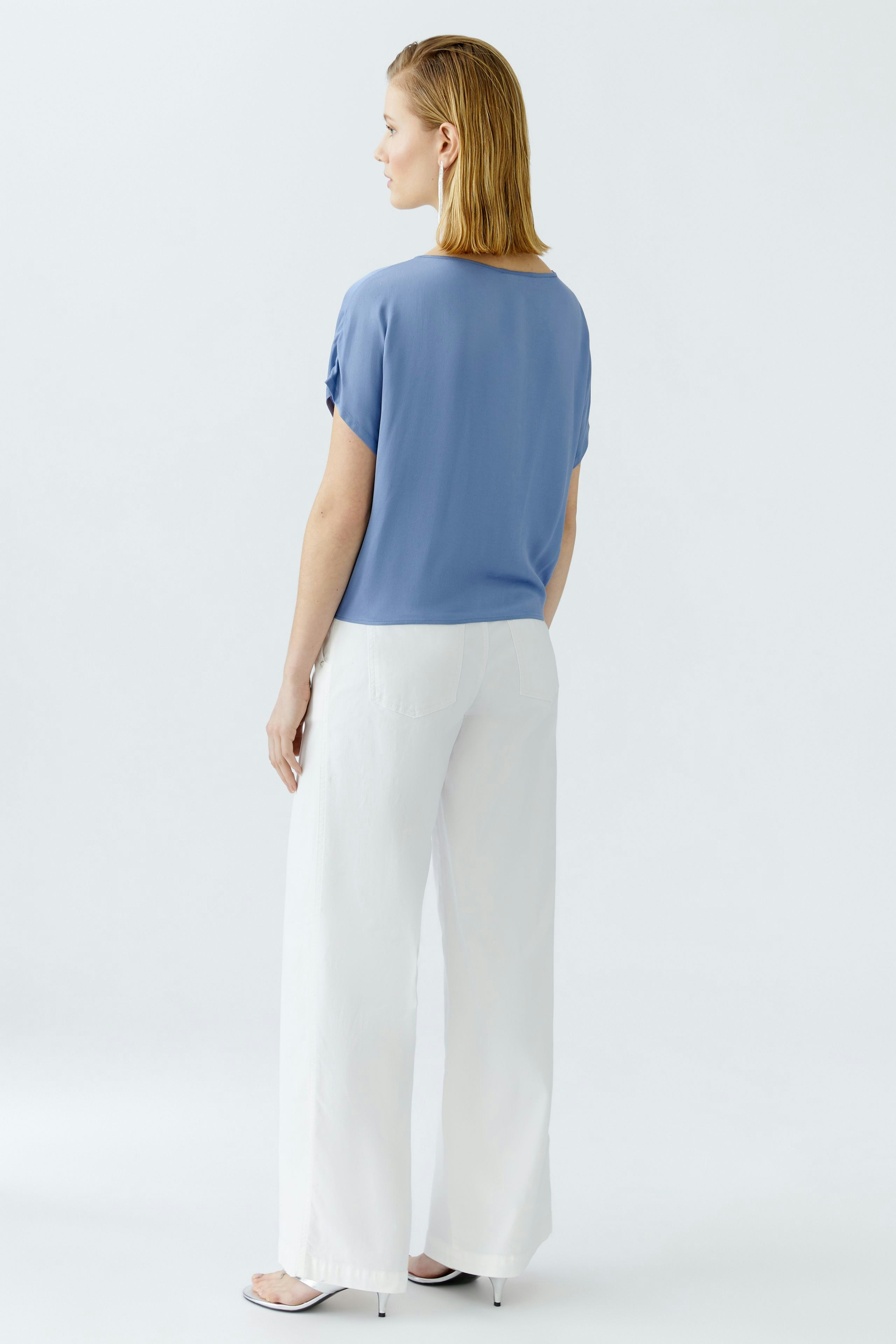 Casual women's blouse: Woman in a light blue blouse paired with white wide-leg pants.