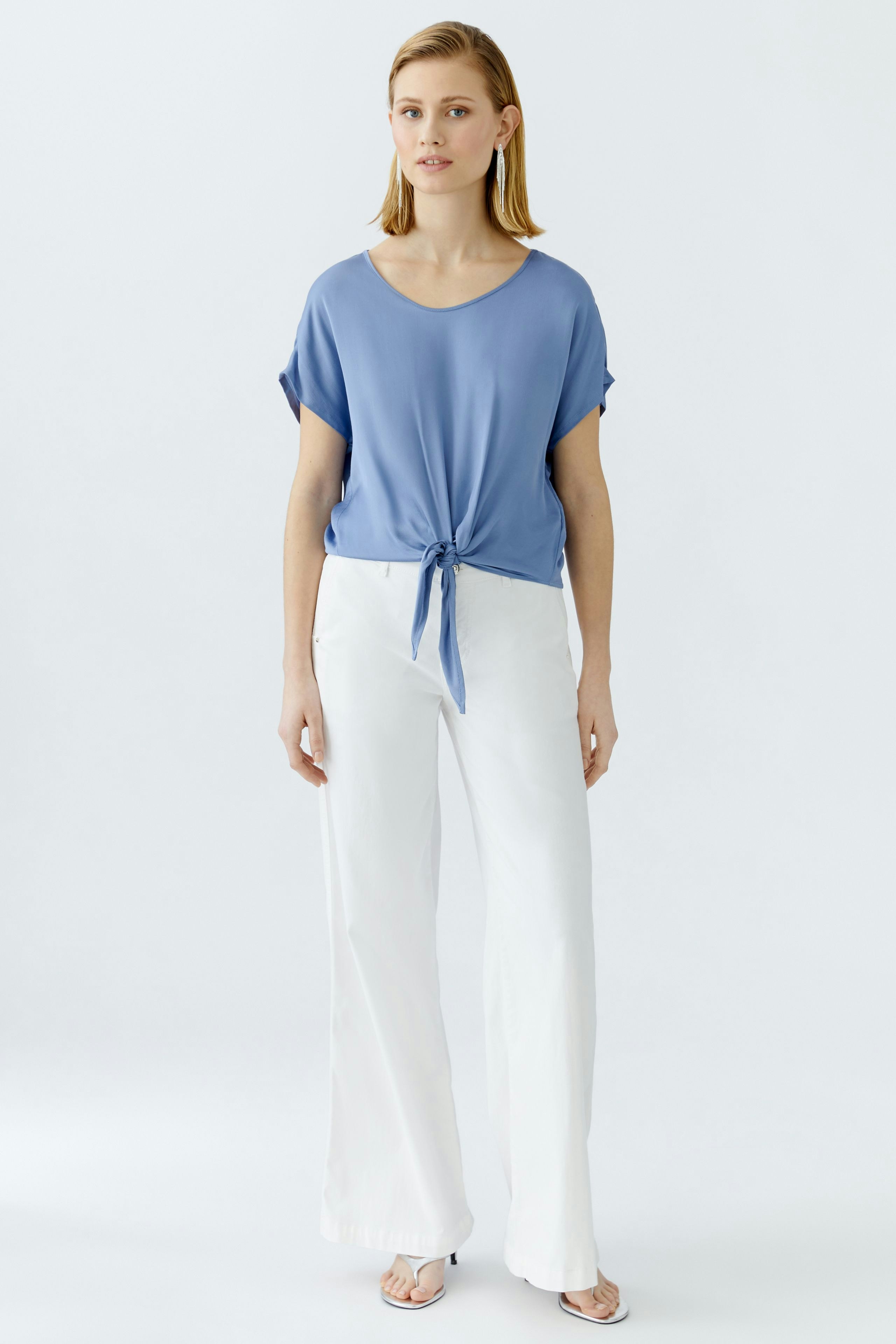 Casual women's blouse: A woman in a blue tied blouse paired with white wide-leg pants.