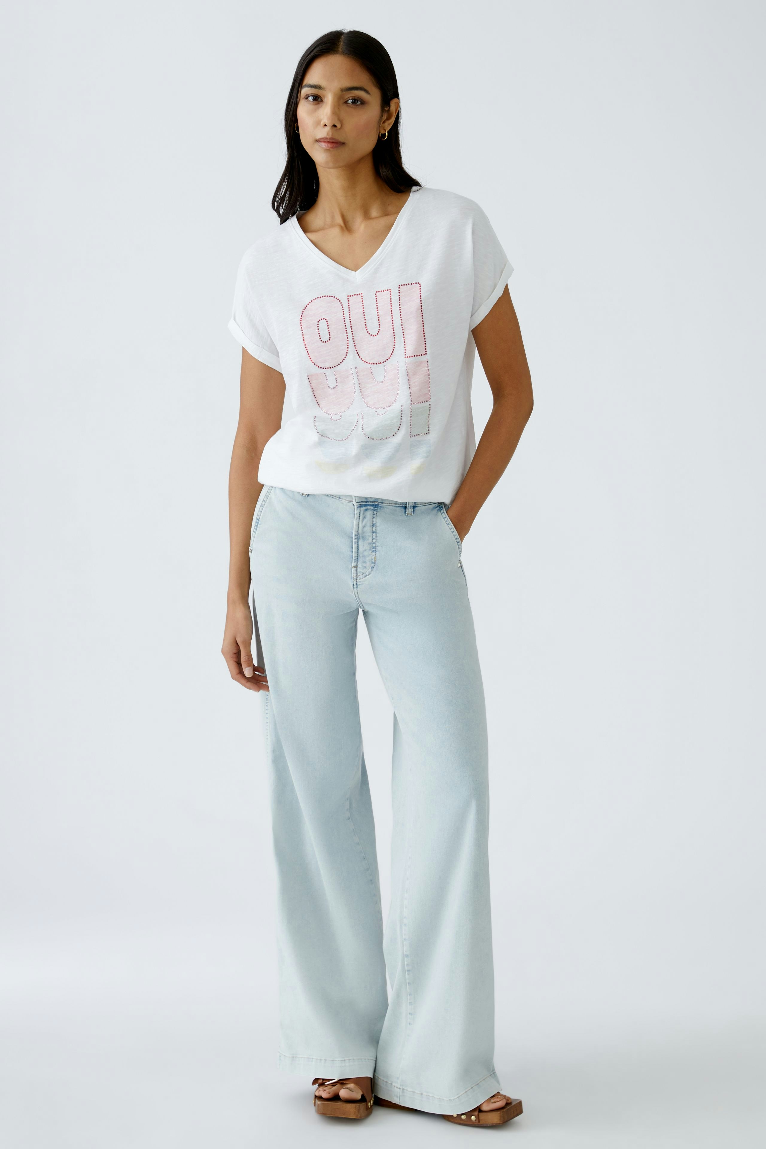 Damen-T-Shirt: Frau in weißem T-Shirt mit buntem 'OUI'-Print und lässigen Jeans.