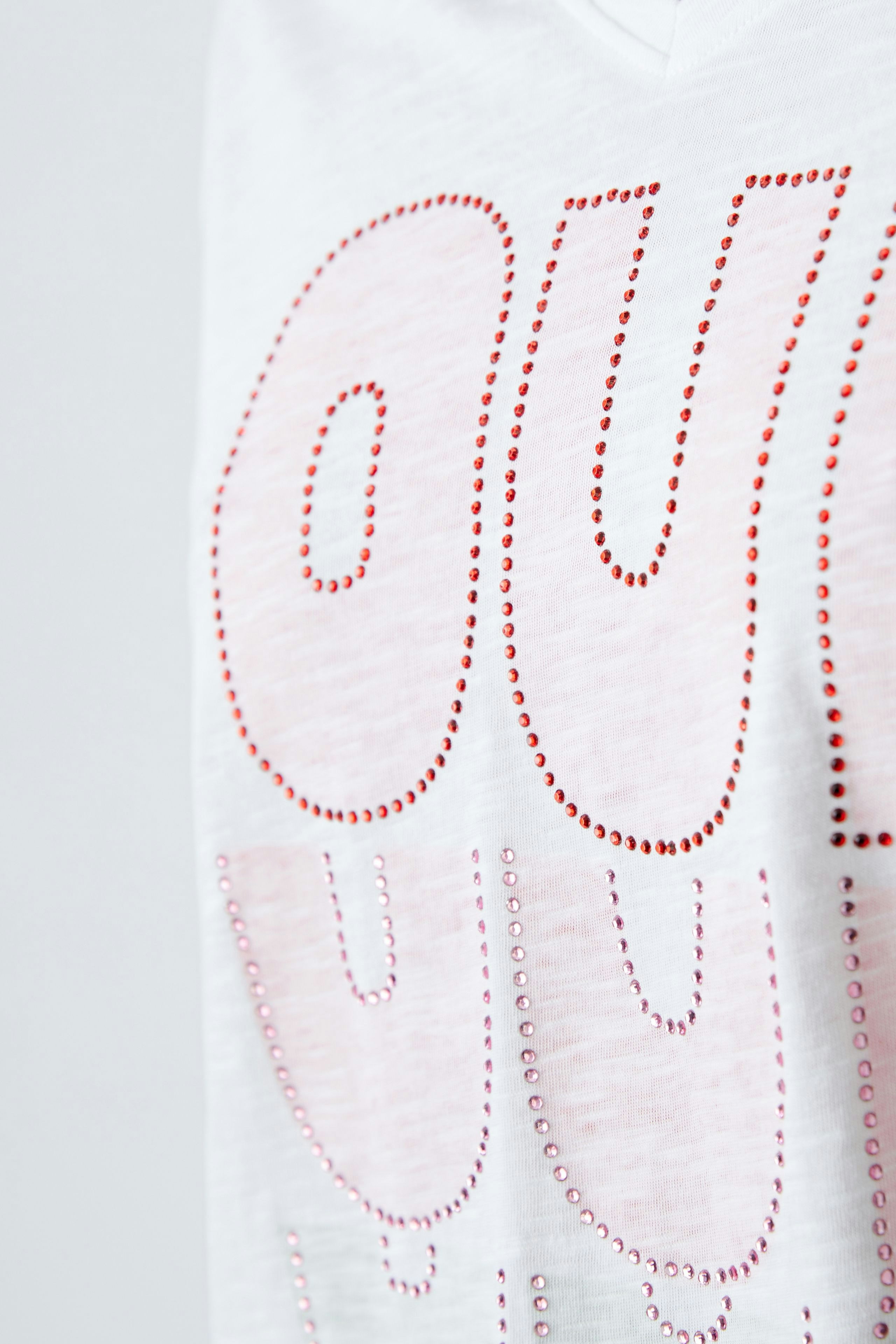 Weißes Damen-T-Shirt mit glänzenden roten Applikationen, lässig und modern.