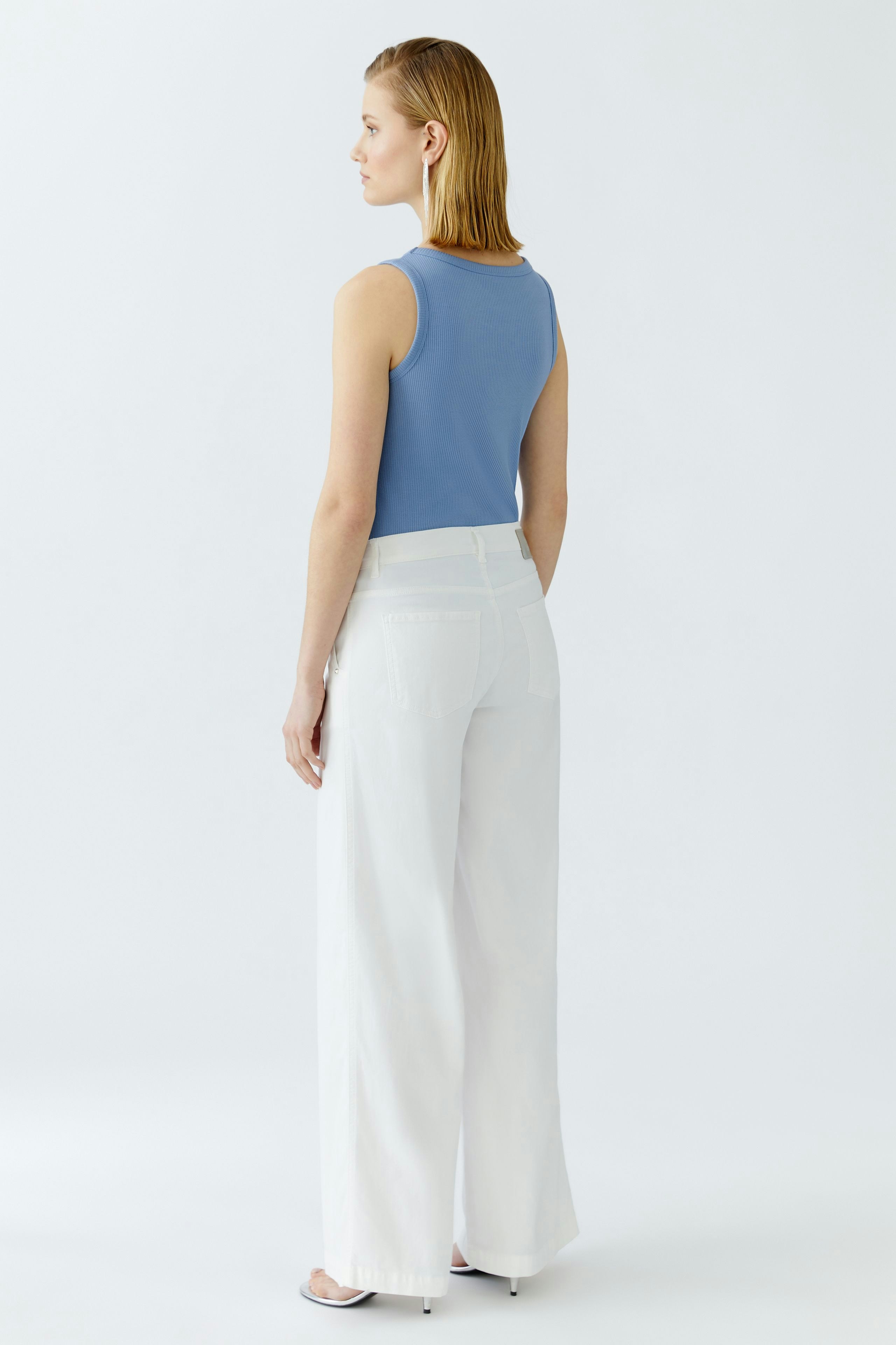 Flared jeans: Woman in white flared jeans and blue tank top, showcasing a relaxed fit.