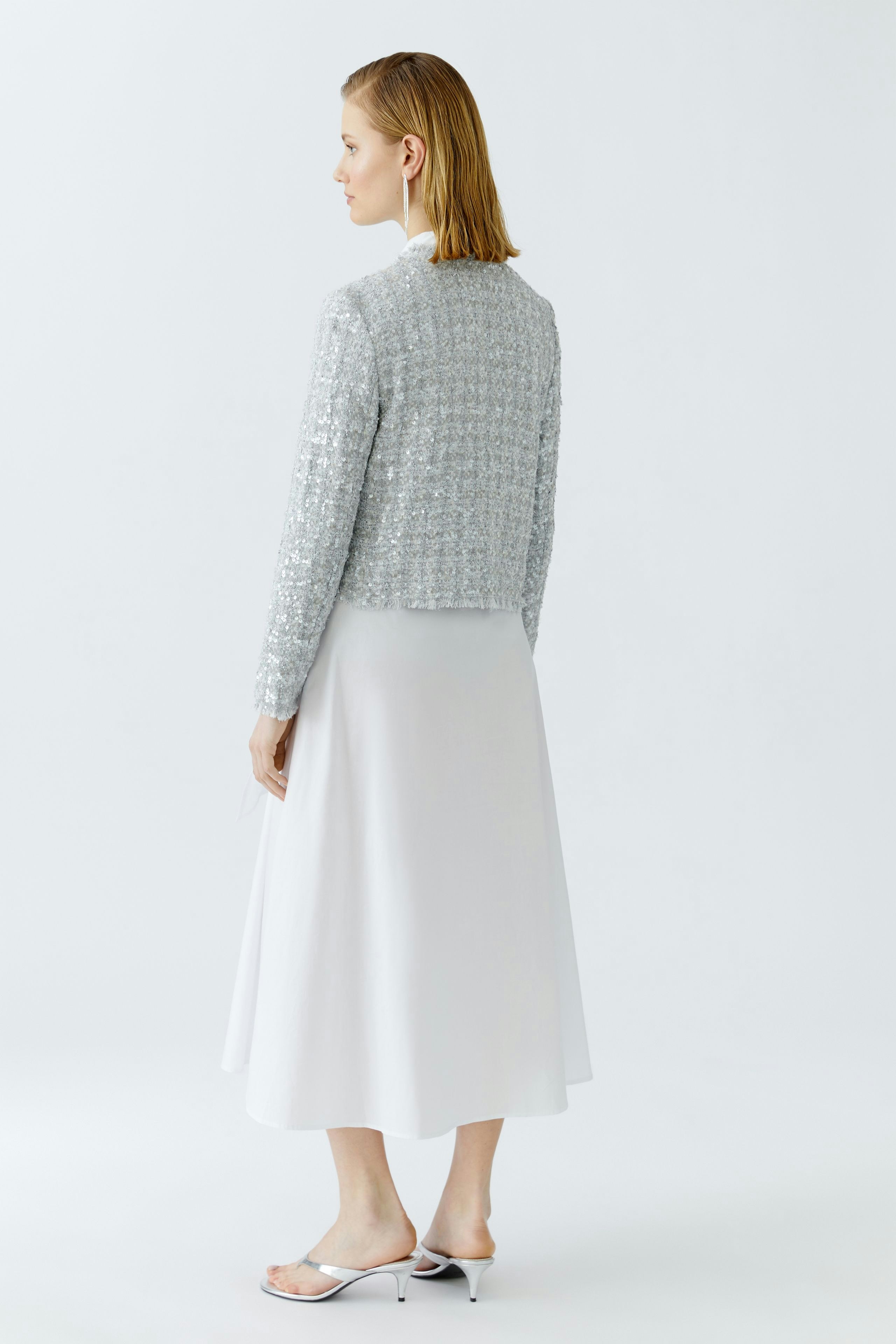 Damen-Jacke: Frau mit silberner, strukturierter Jacke und weißem Rock von hinten.