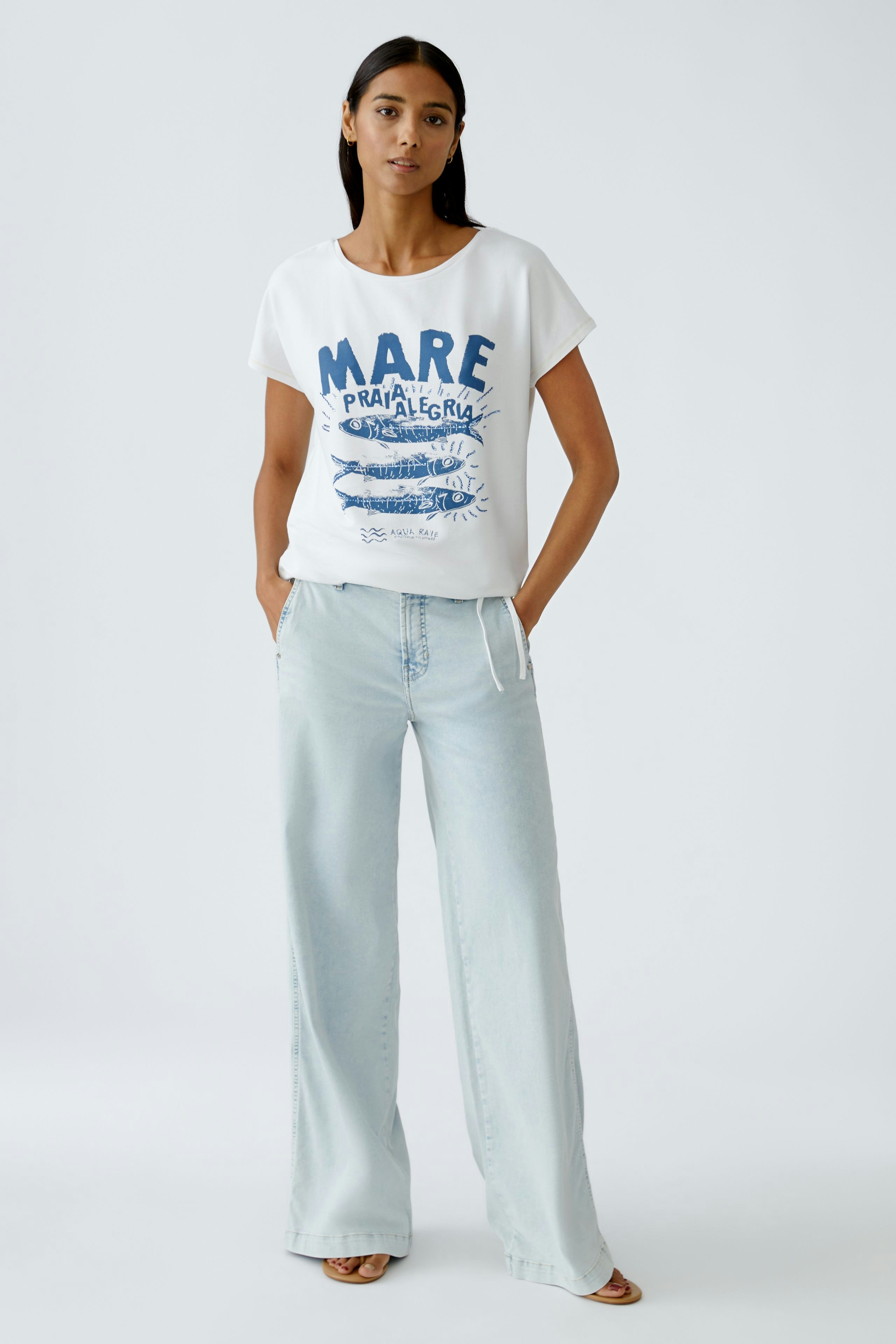 Damen-T-Shirt in Weiß mit blauem Druck, lässig kombiniert mit weißen Hosen.