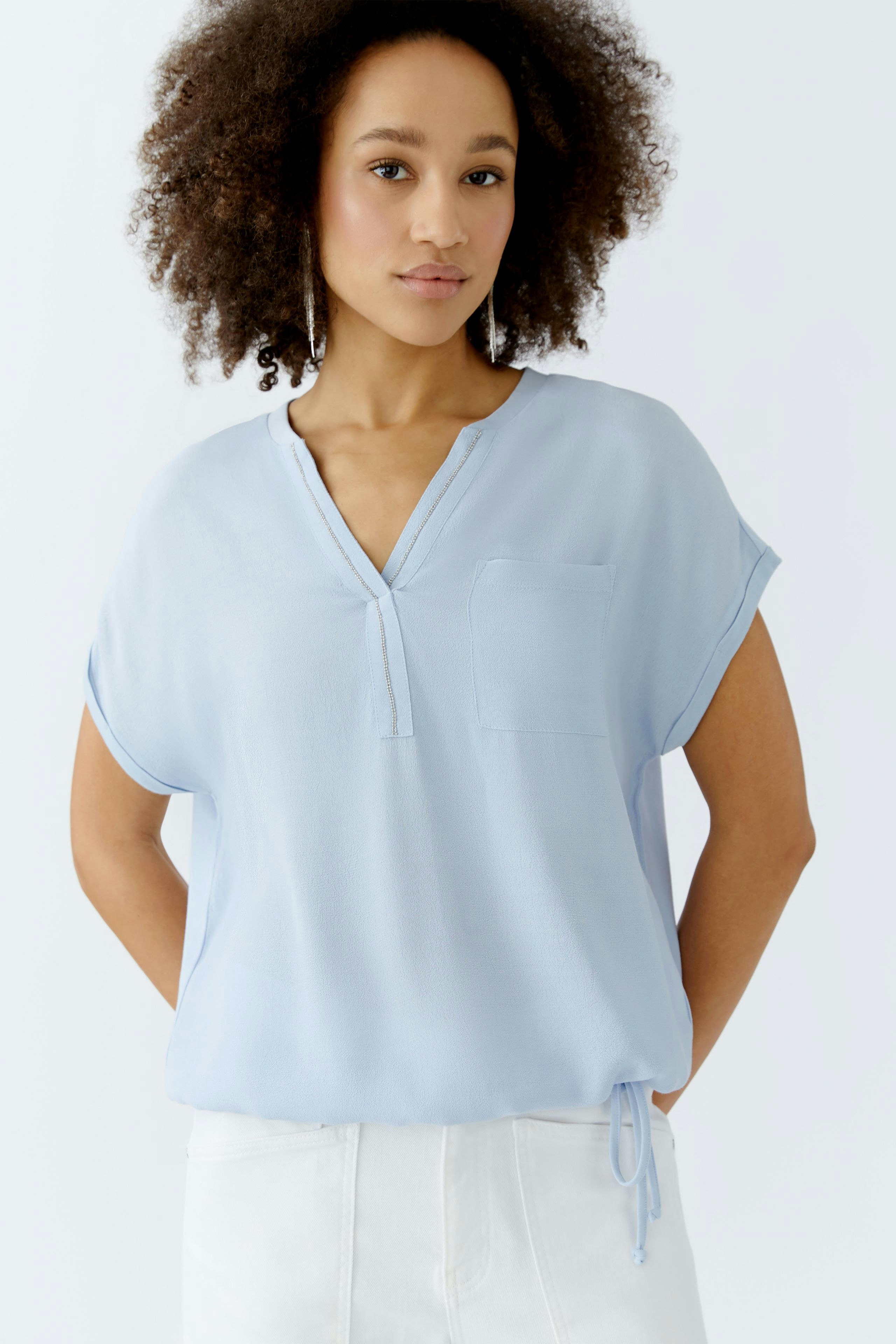 Leichtes Blusenshirt: Frau trägt ein hellblaues Shirt mit kurzer Arm und Brusttasche.