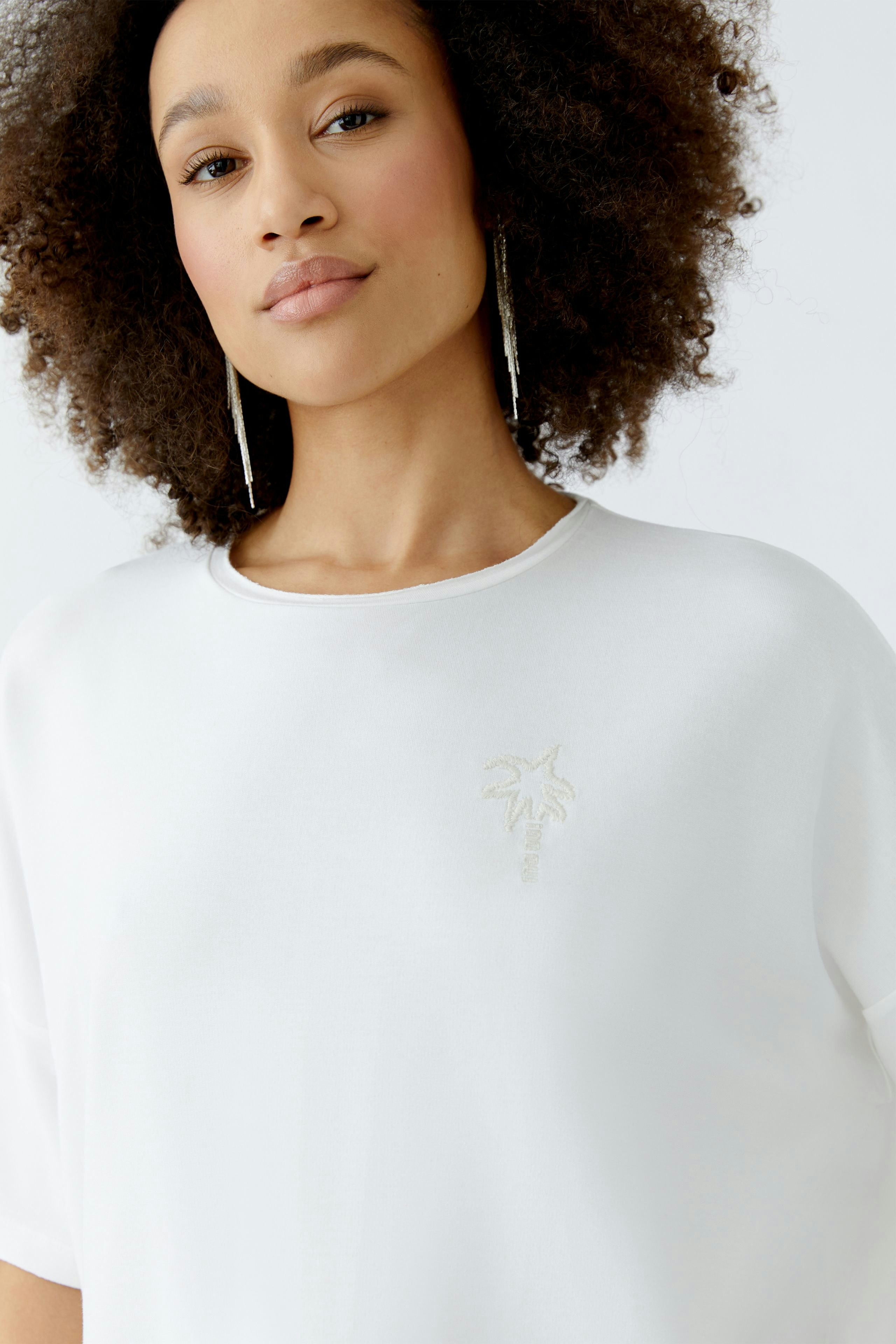 Bequemer Damen-Sweatshirt: Frau mit lockigem Haar trägt ein weißes Sweatshirt mit dezentem Palmendruck.