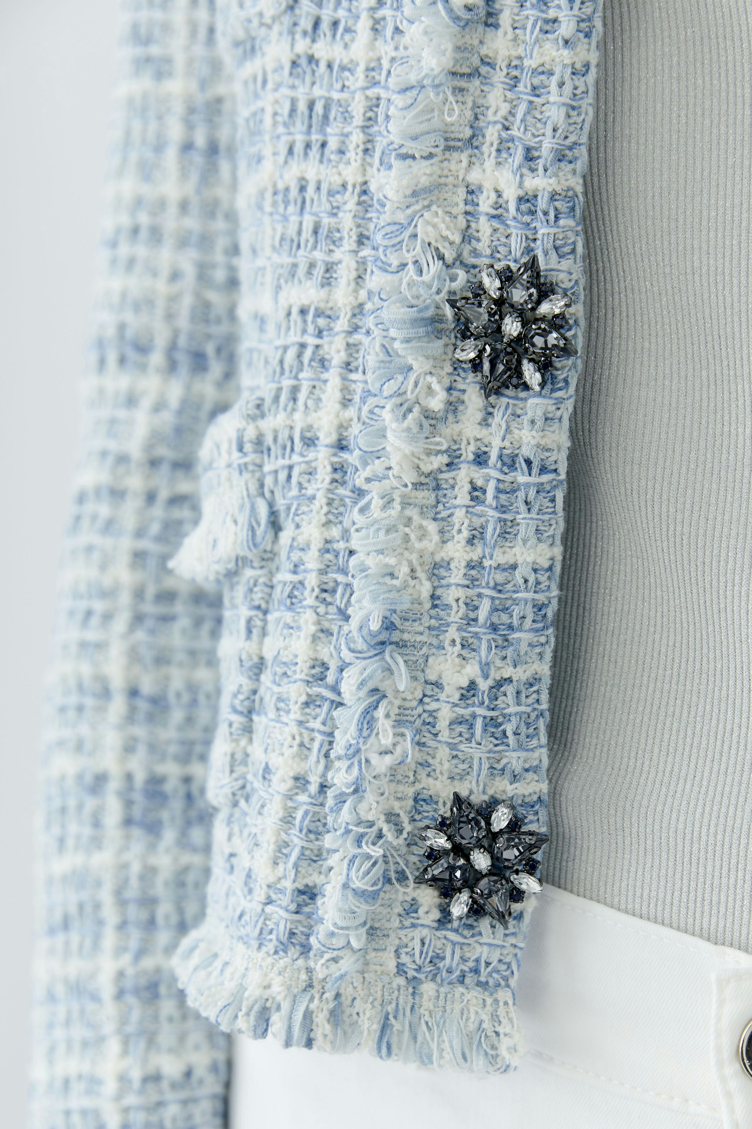 Casual women's cardigan: Close-up of a blue textured cardigan with decorative flowers.