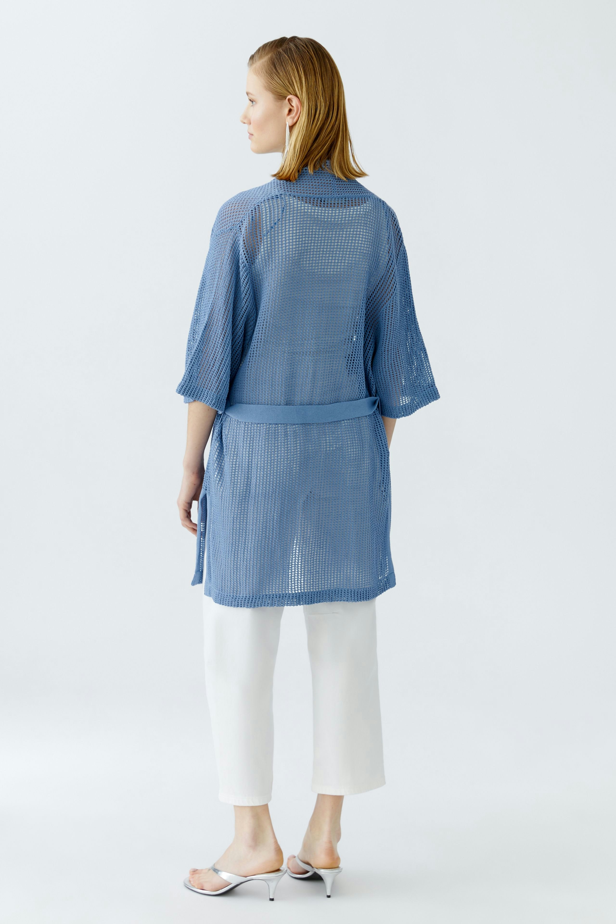 Light blue cardigan: Woman in a loose-knit cardigan with a belt, paired with white pants.