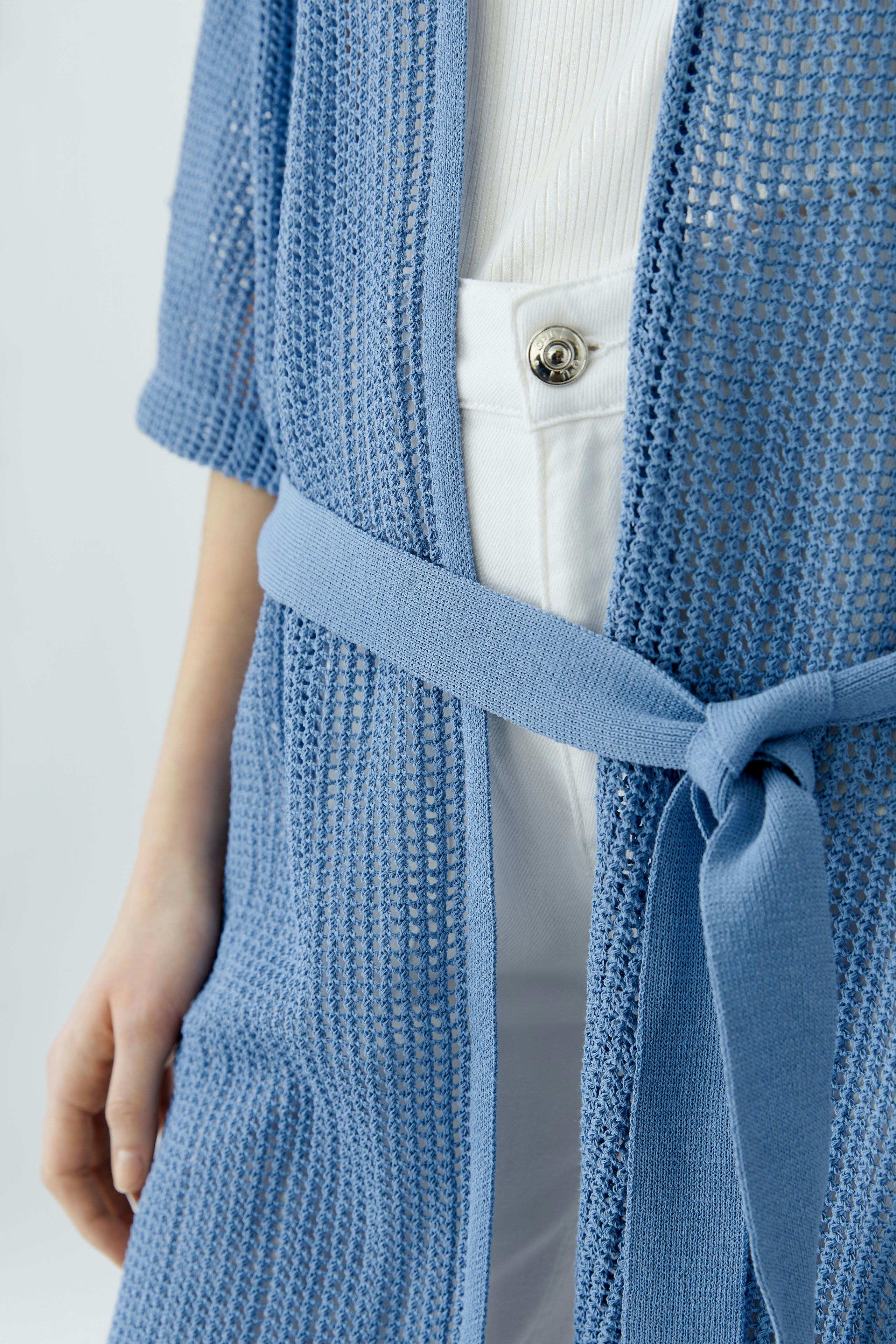 Light blue cardigan: Woman wearing a knitted cardigan with a belt, paired with white pants.