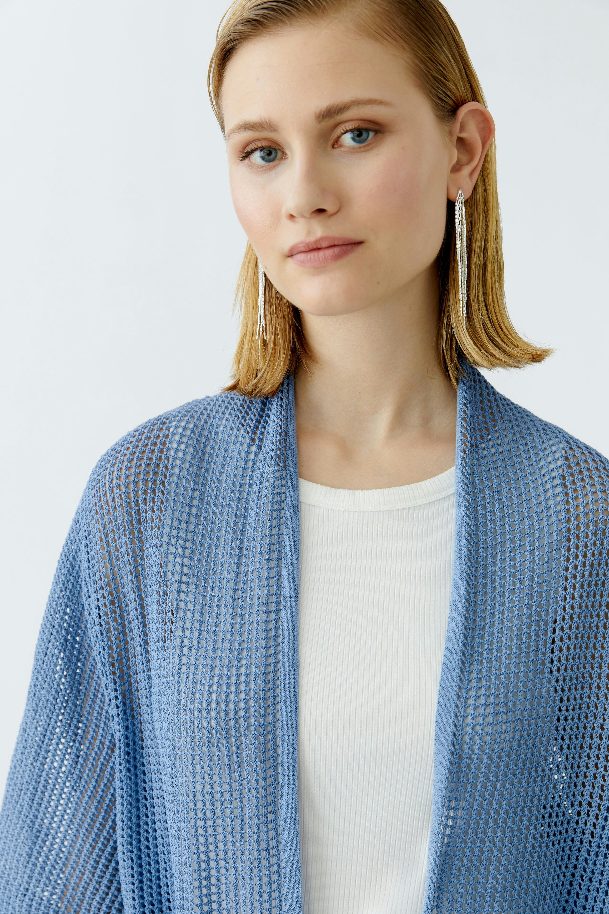 Light blue cardigan: Young woman wearing a loose-knit cardigan over a white top, looking relaxed.