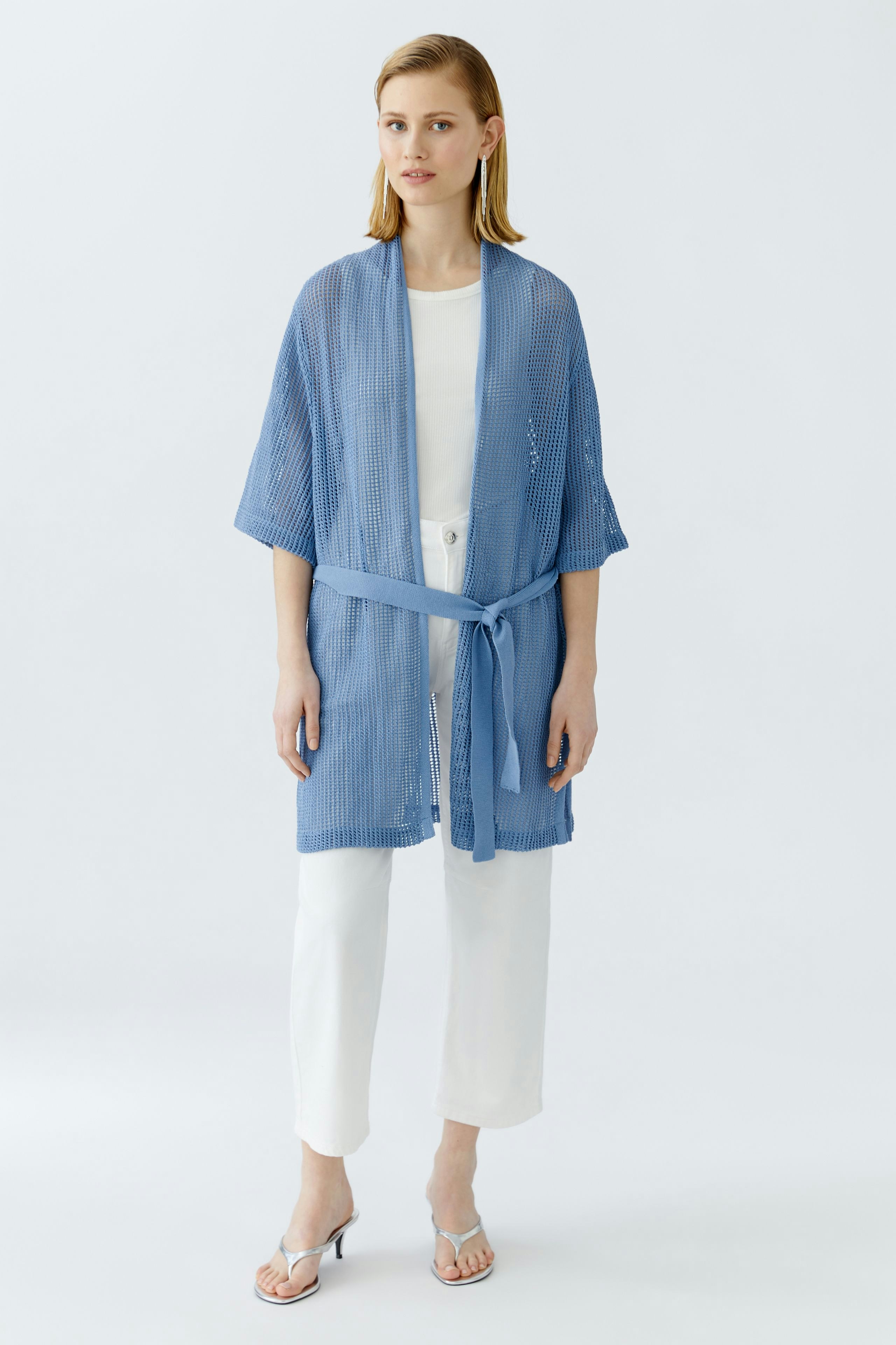 Light blue cardigan: Woman in a loose-knit cardigan with a tie belt, paired with white pants.