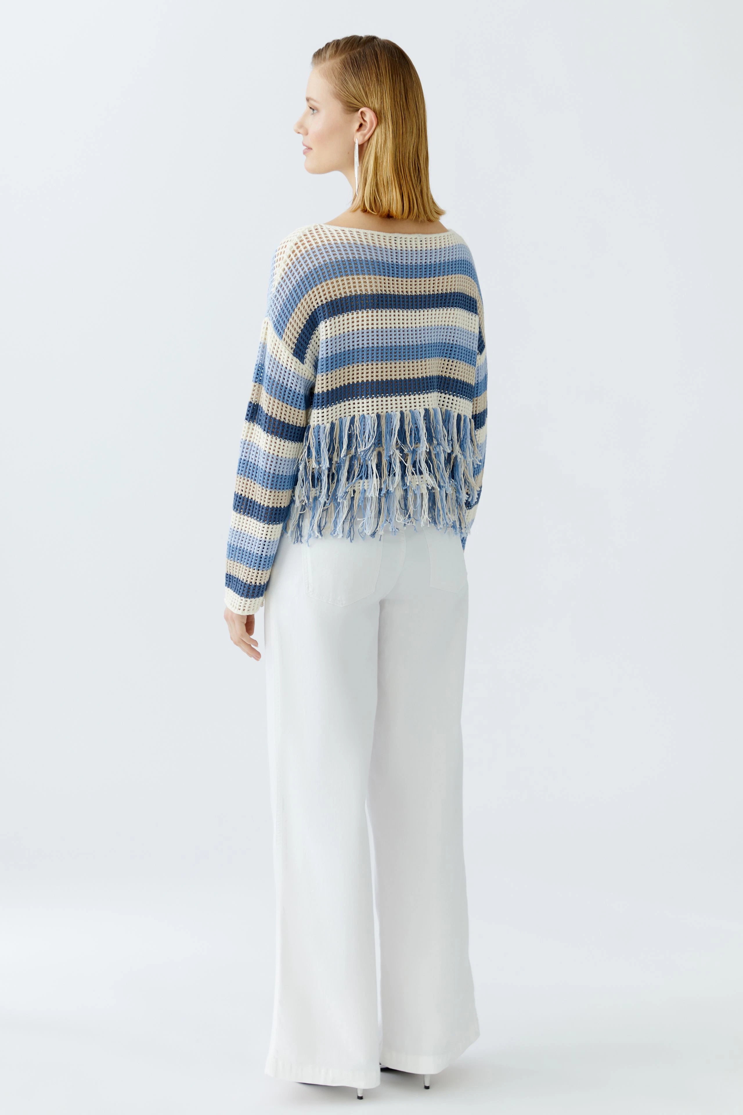 Casual women's pullover: A woman in a striped pullover with fringes, paired with wide white pants.
