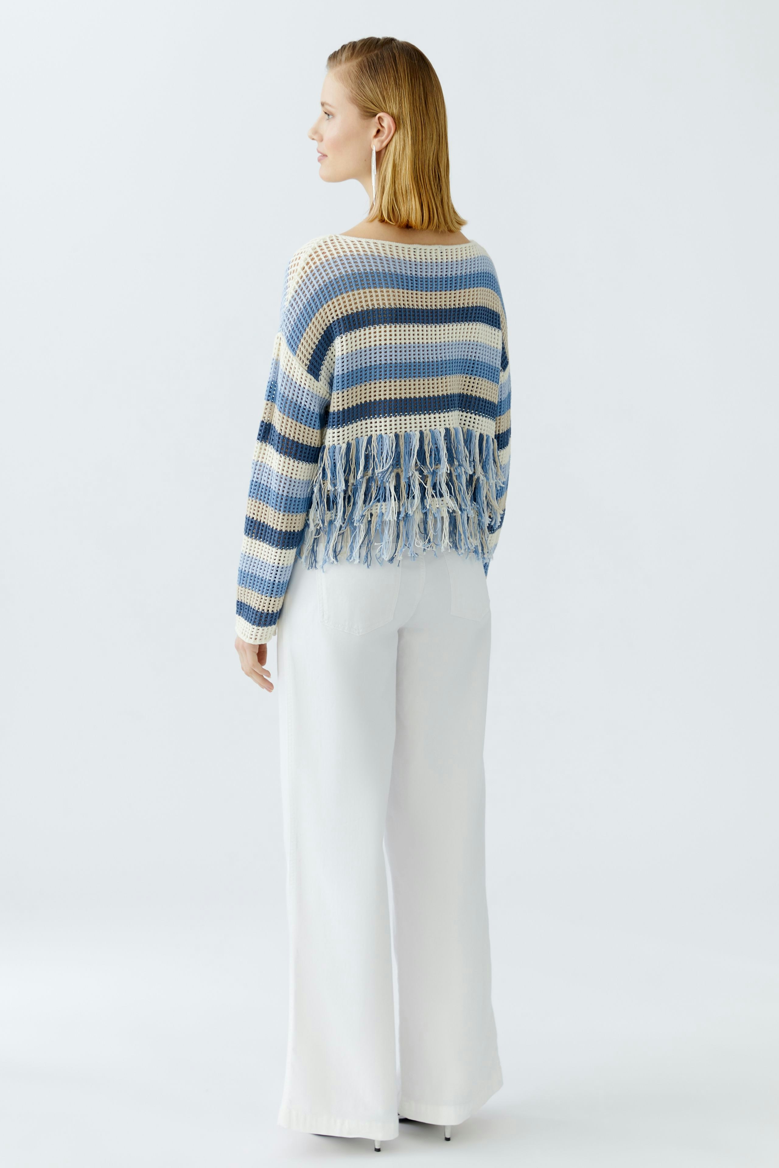 Casual women's pullover: A woman in a striped pullover with fringes, paired with wide white pants.