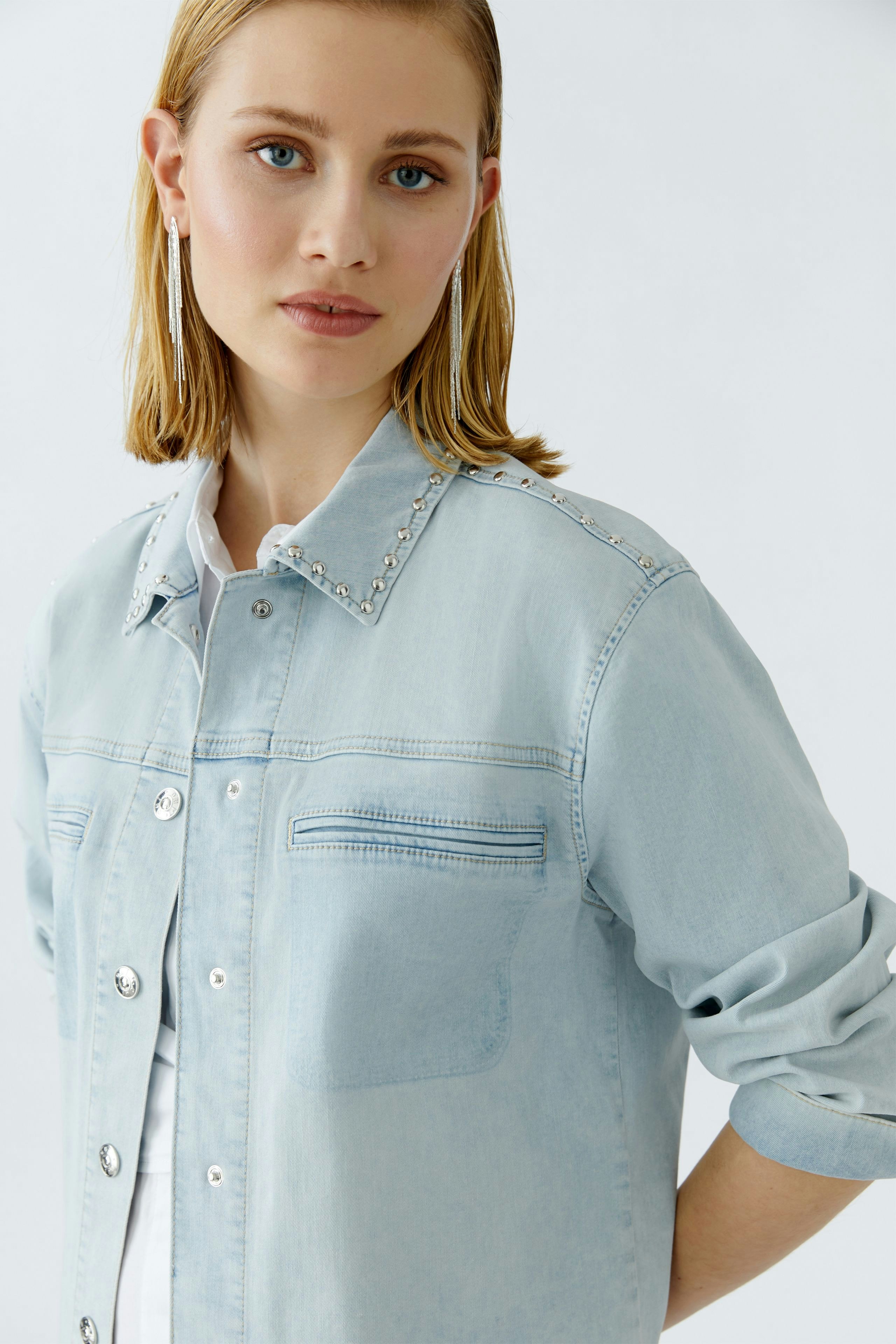 Casual women's denim jacket: A woman in a light blue jacket with decorative studs and rolled-up sleeves.