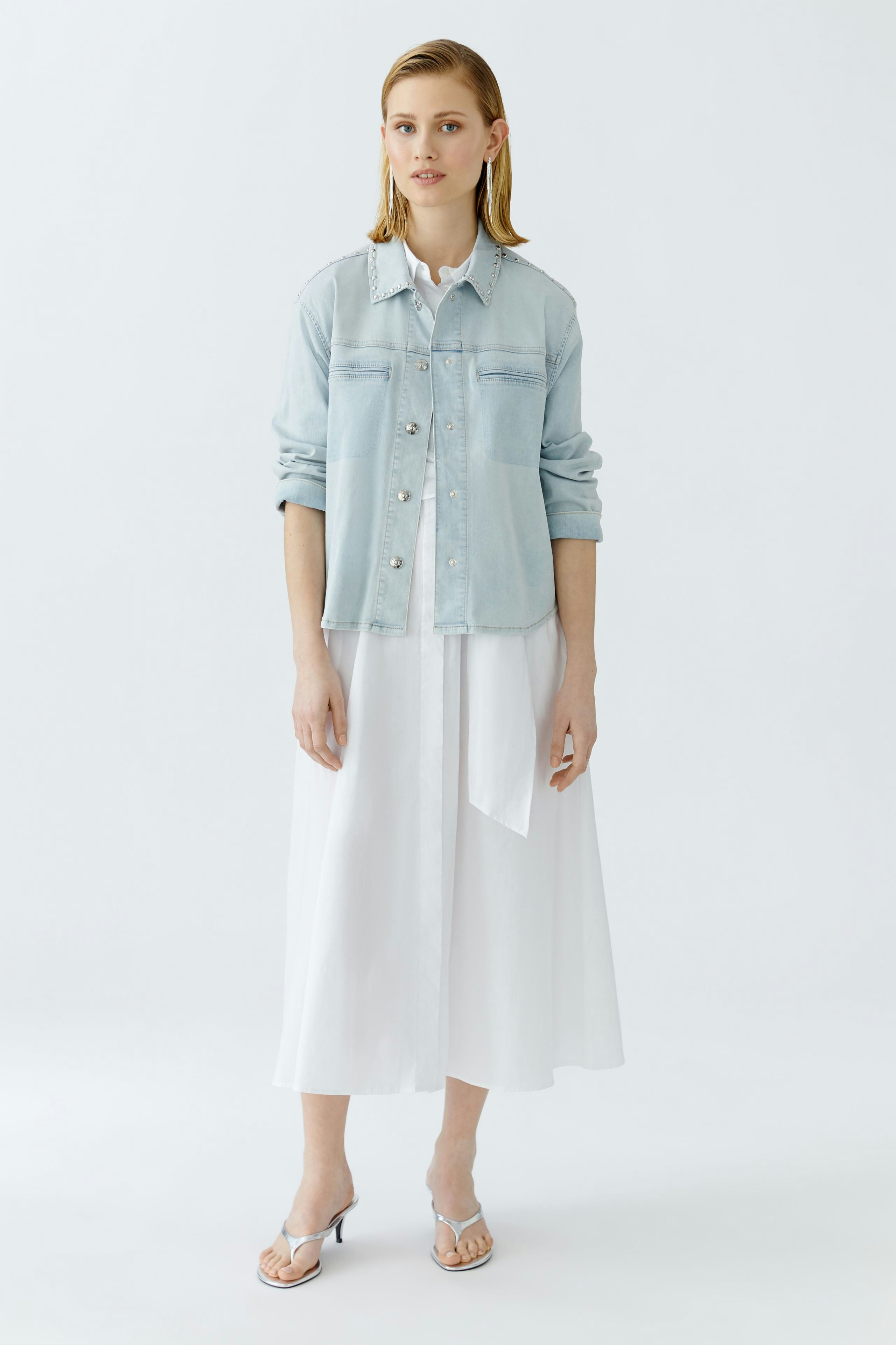 Casual women's denim jacket: A woman in a light blue jacket over a white dress stands confidently.