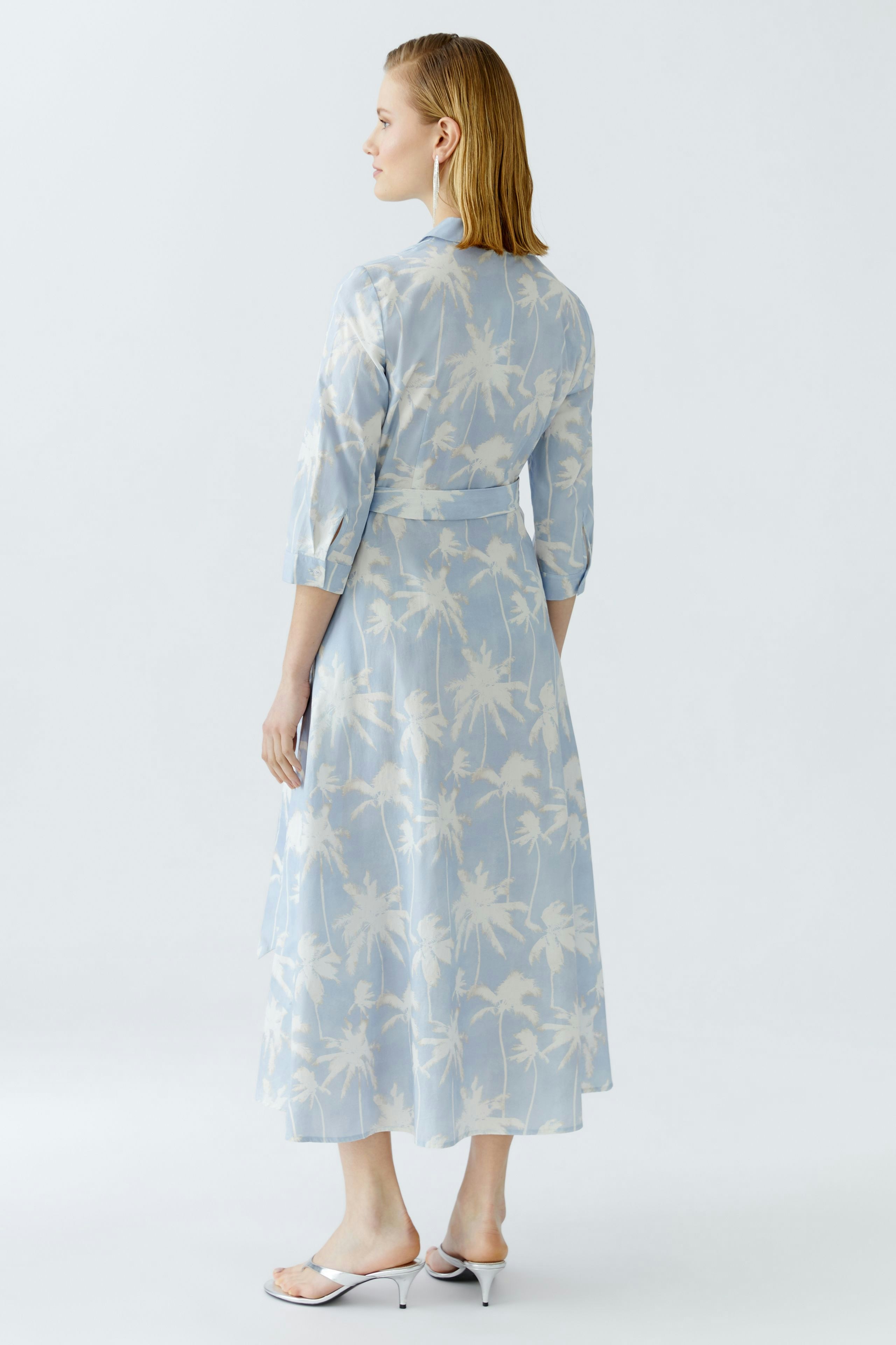 Wickelkleid: Frau in einem hellblauen Kleid mit Palmenmuster, lässig und bequem.