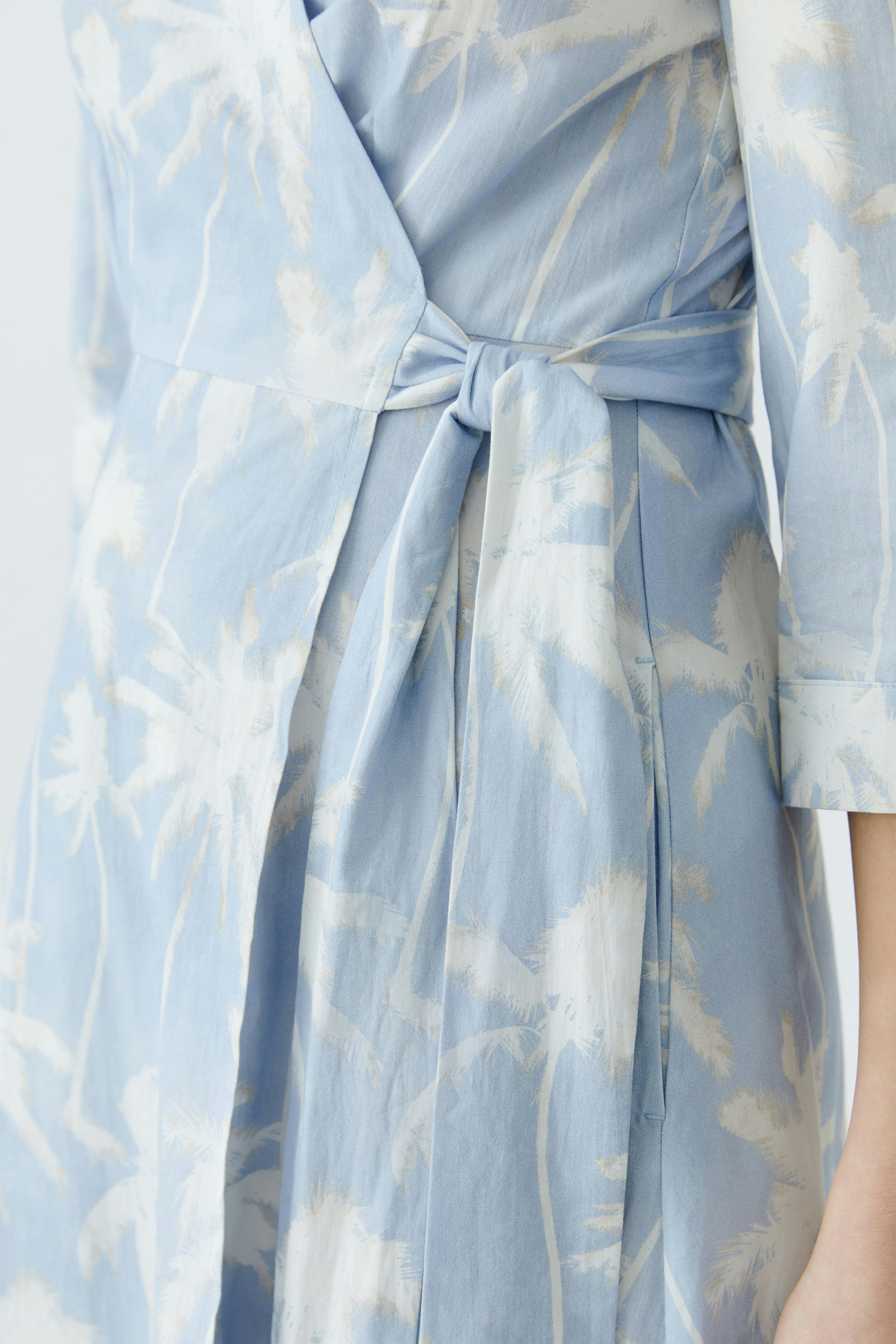 Wickelkleid: Damenmodell in hellblau mit floralem Muster und tailliertem Schnitt.